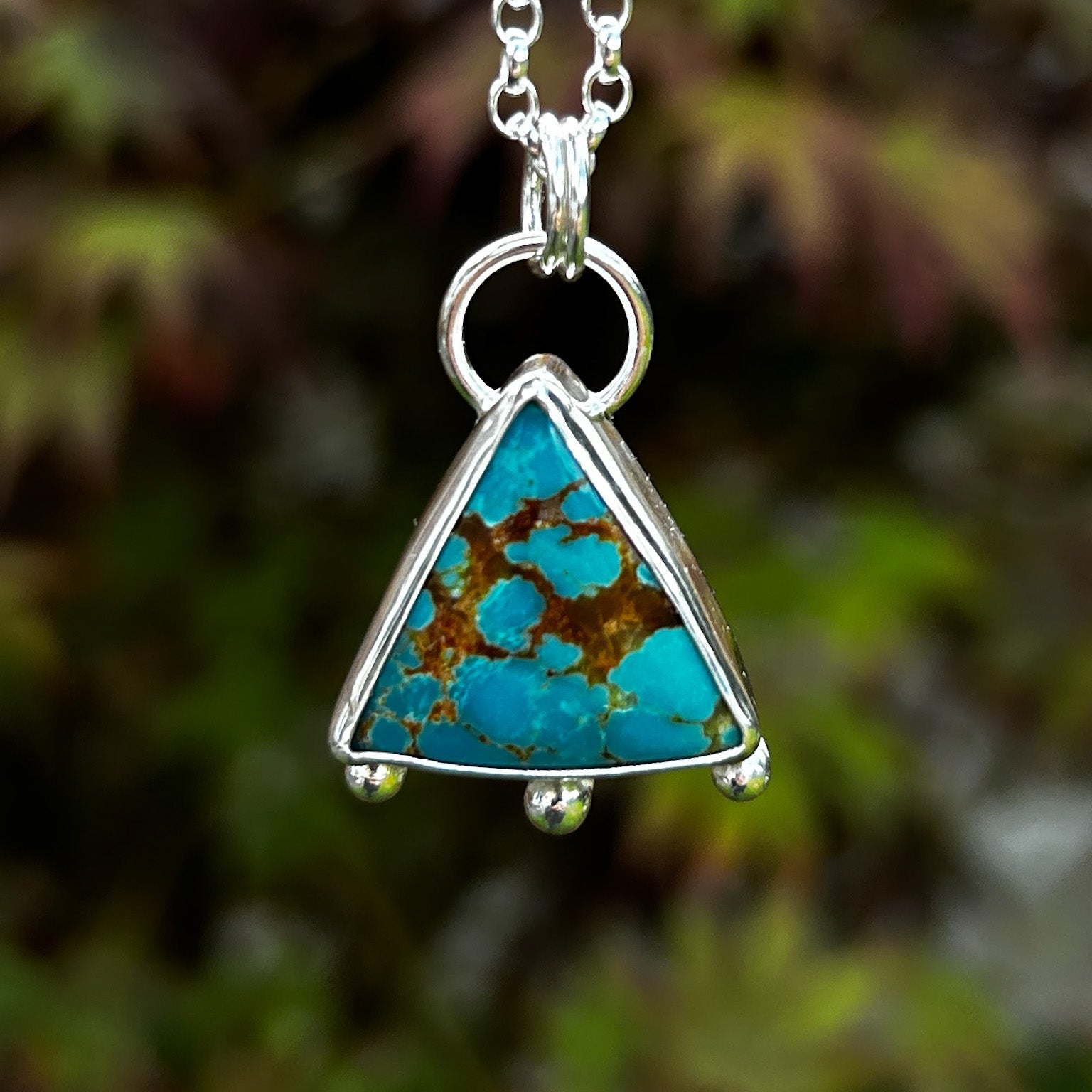 Turquoise pendant on a silver chain against a blurred natural background