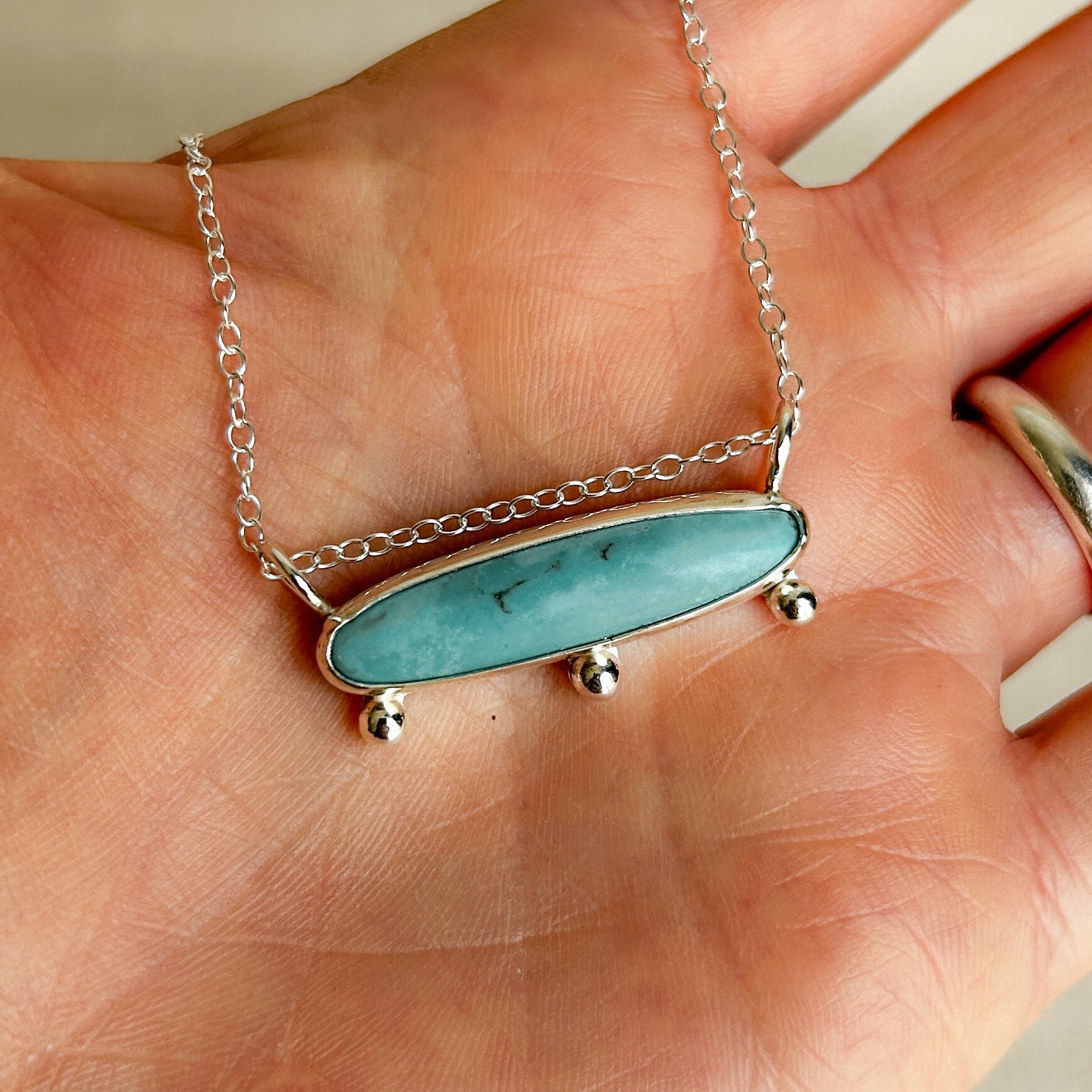 Model holding a turquoise pendant necklace with sterling silver chain