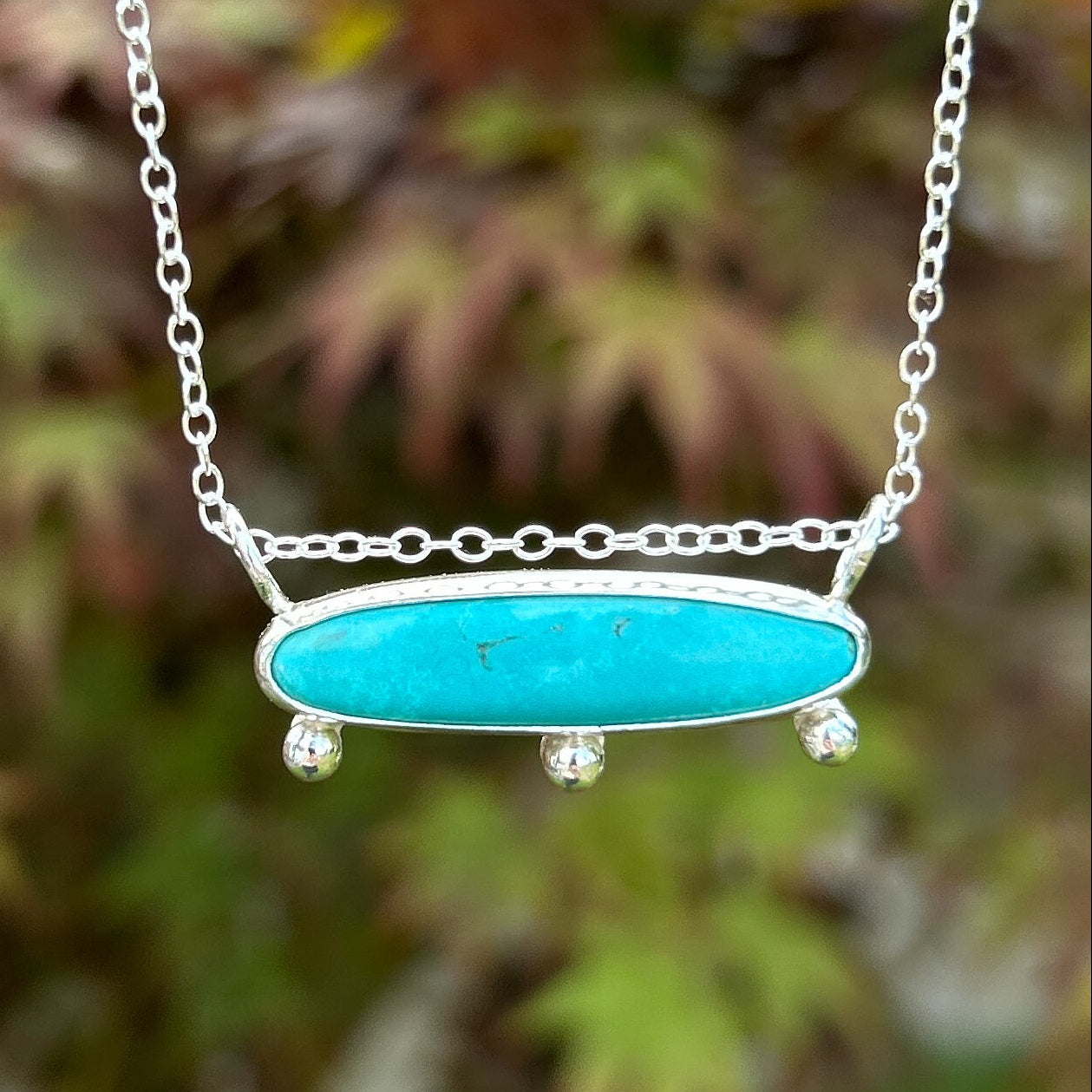 Turquoise choker necklace with silver chain against a blurred natural background