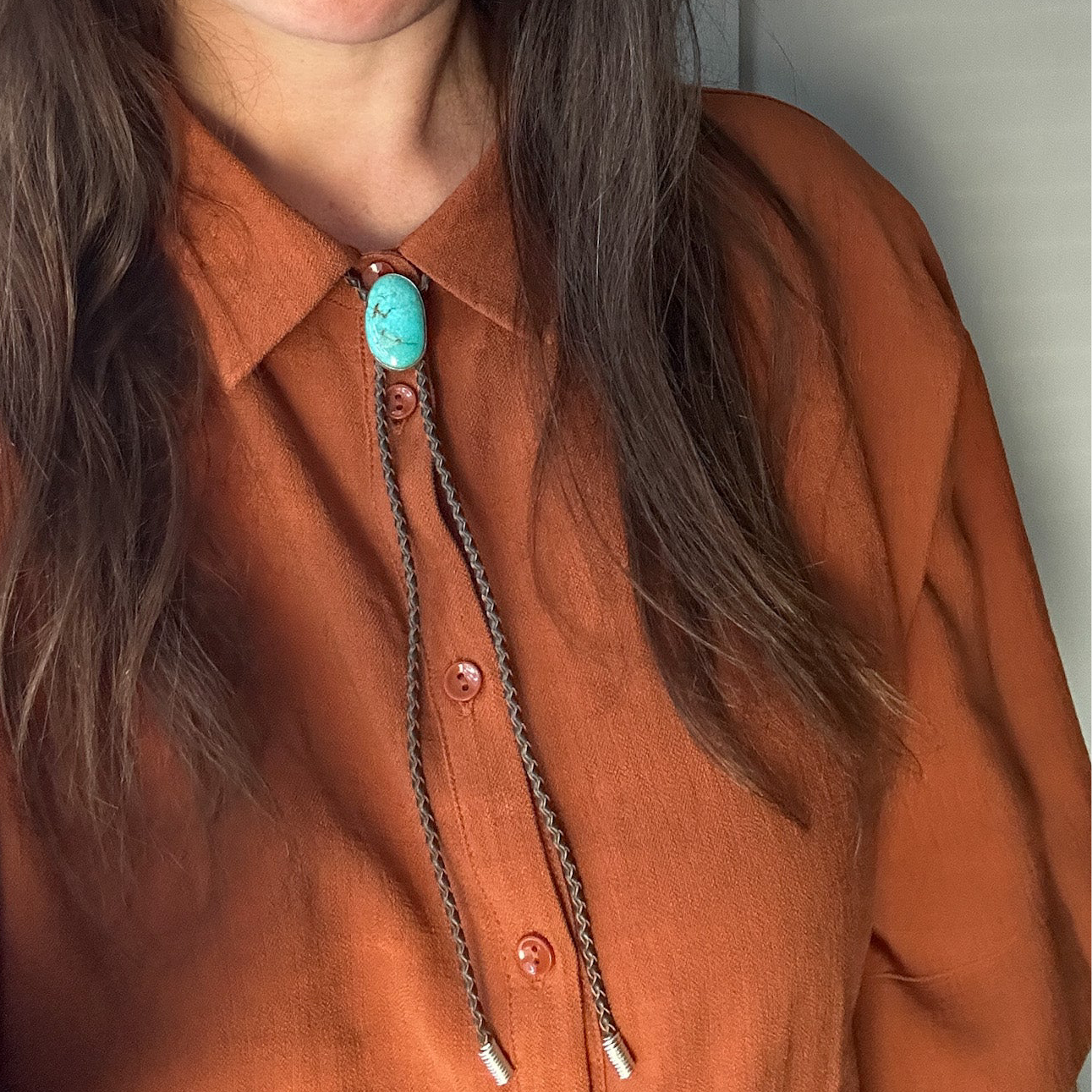 Turquoise bolo tie show on model wearing a rust coloured shirt.