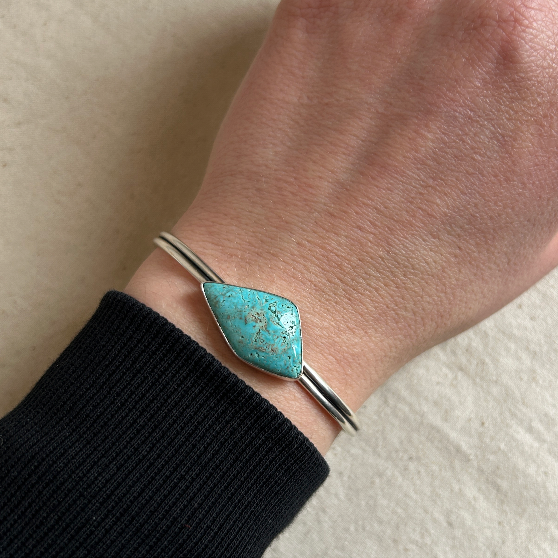 Kite shaped turquoise gemstone sitting on a double-band silver cuff