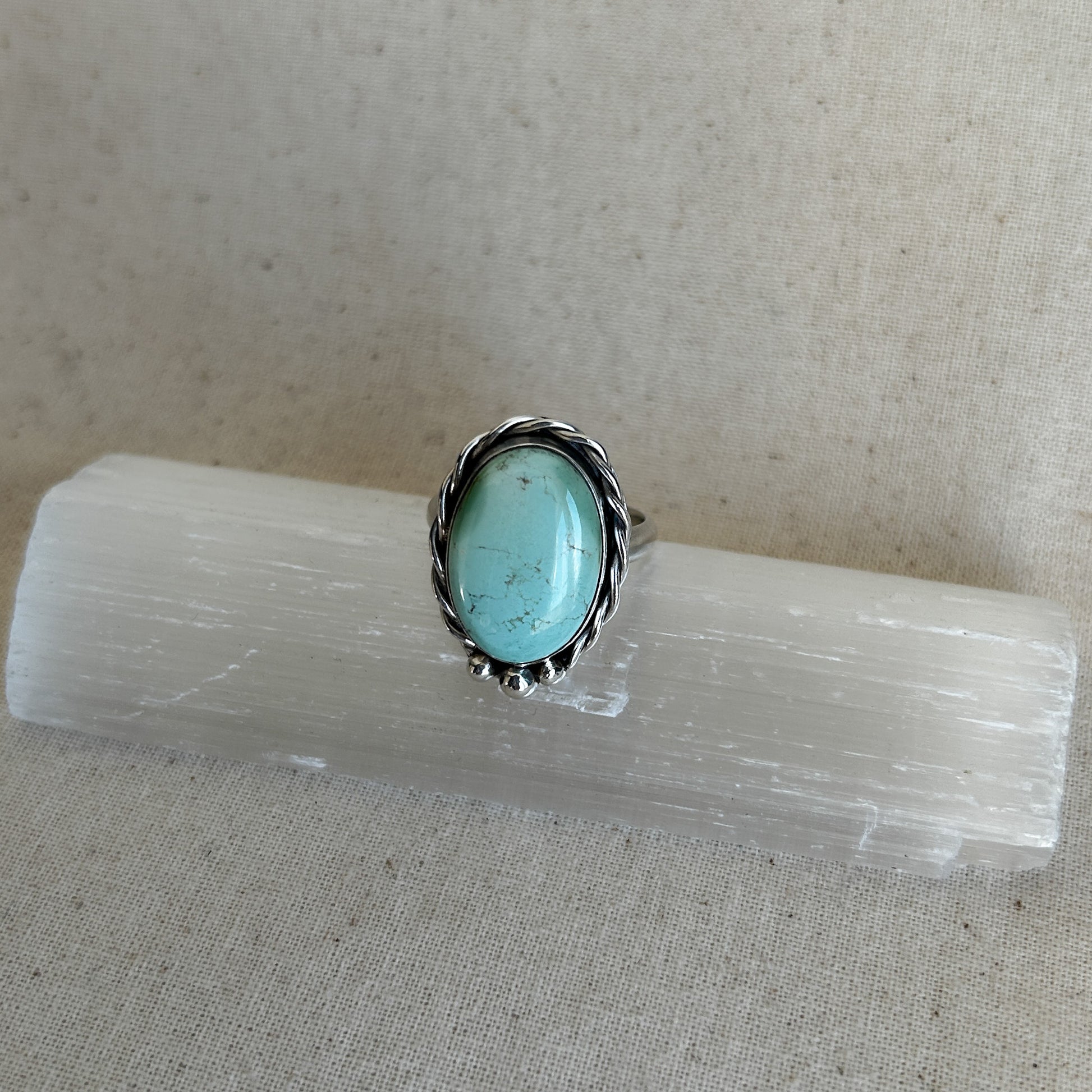 Turquoise gemstone ring with silver border on a crystal display stand