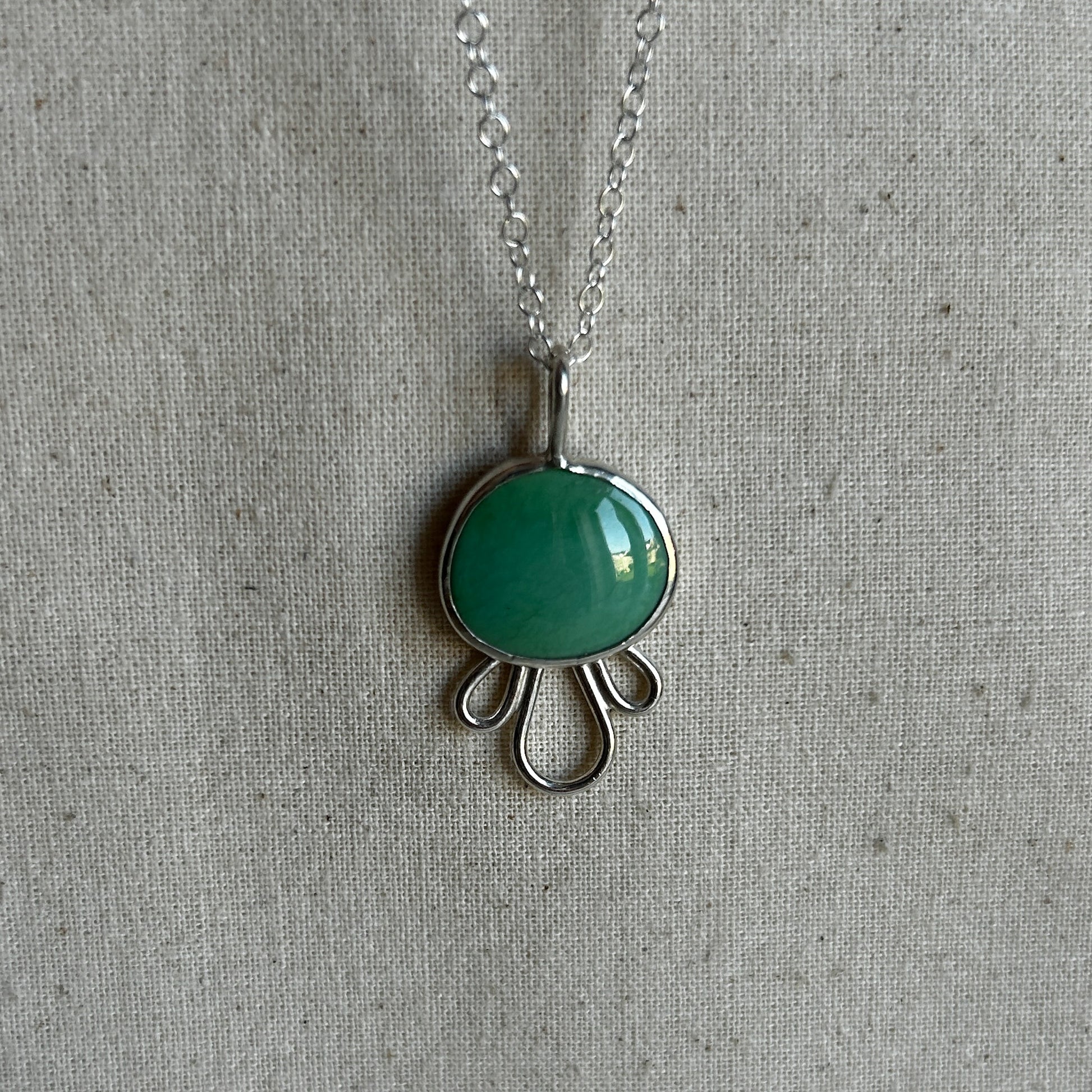 Green turquoise pendant with petal-like border on silver chain against grey background