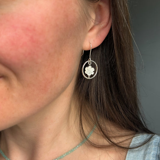 Silver dangle earrings with white flower in centre worn in ear of model