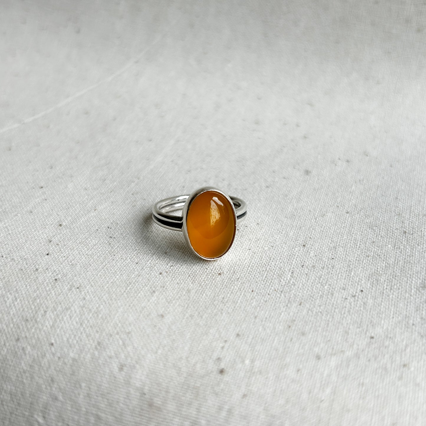 A yellow chalcedony ring with a simple silver setting on a textured white background.