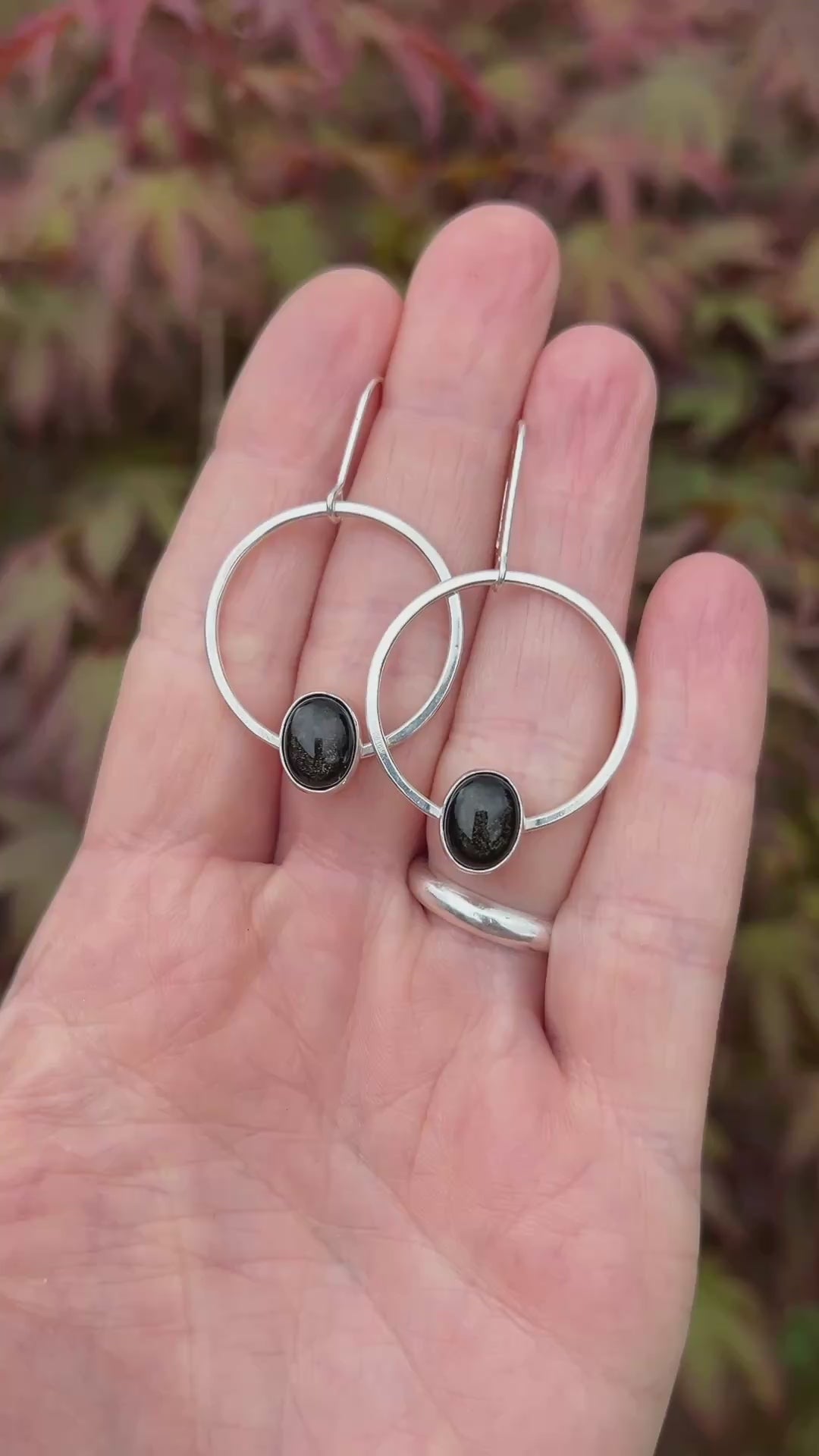 Silver and obsidian earrings held in hand against a natural blurred background