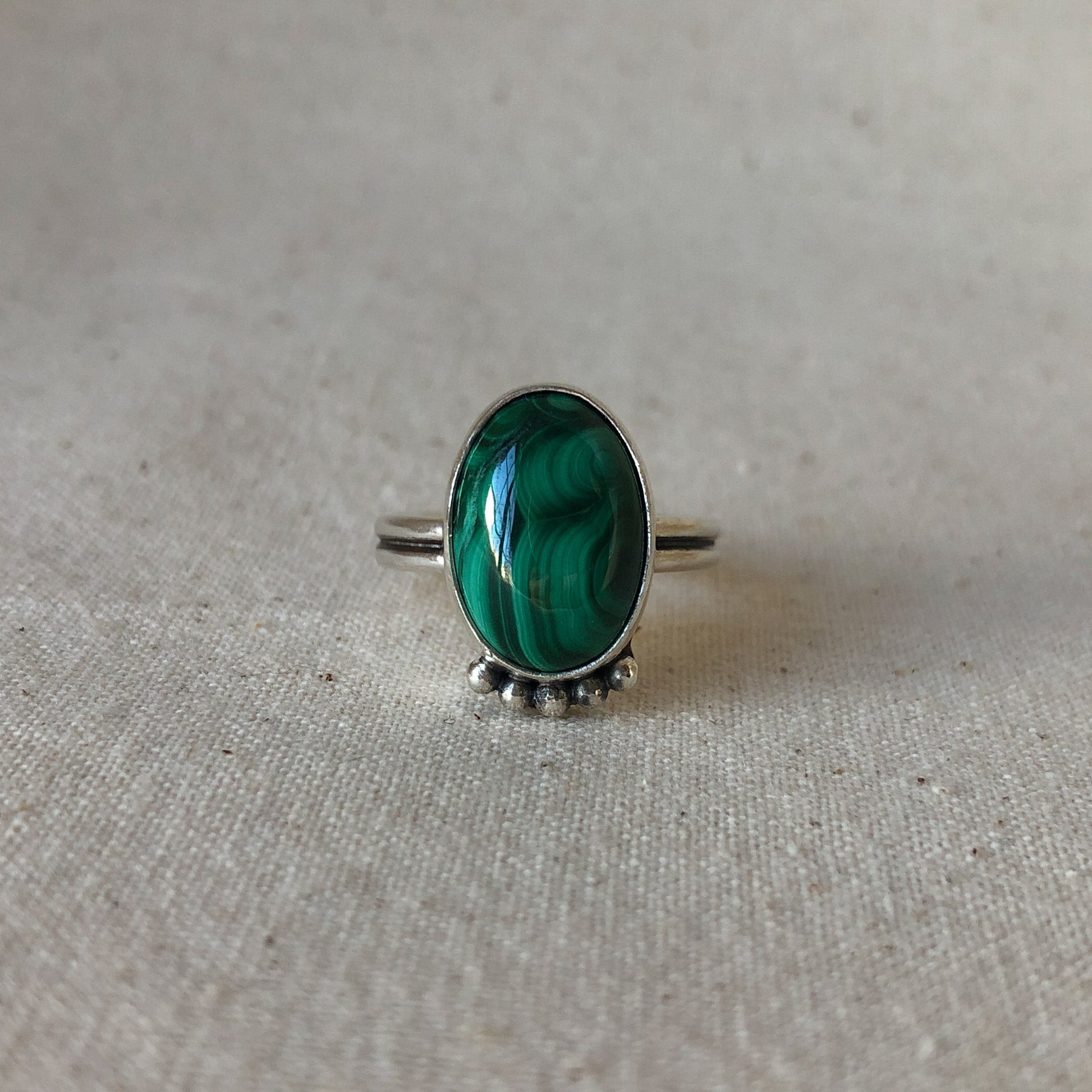 Malachite gemstone ring with silver band on grey background