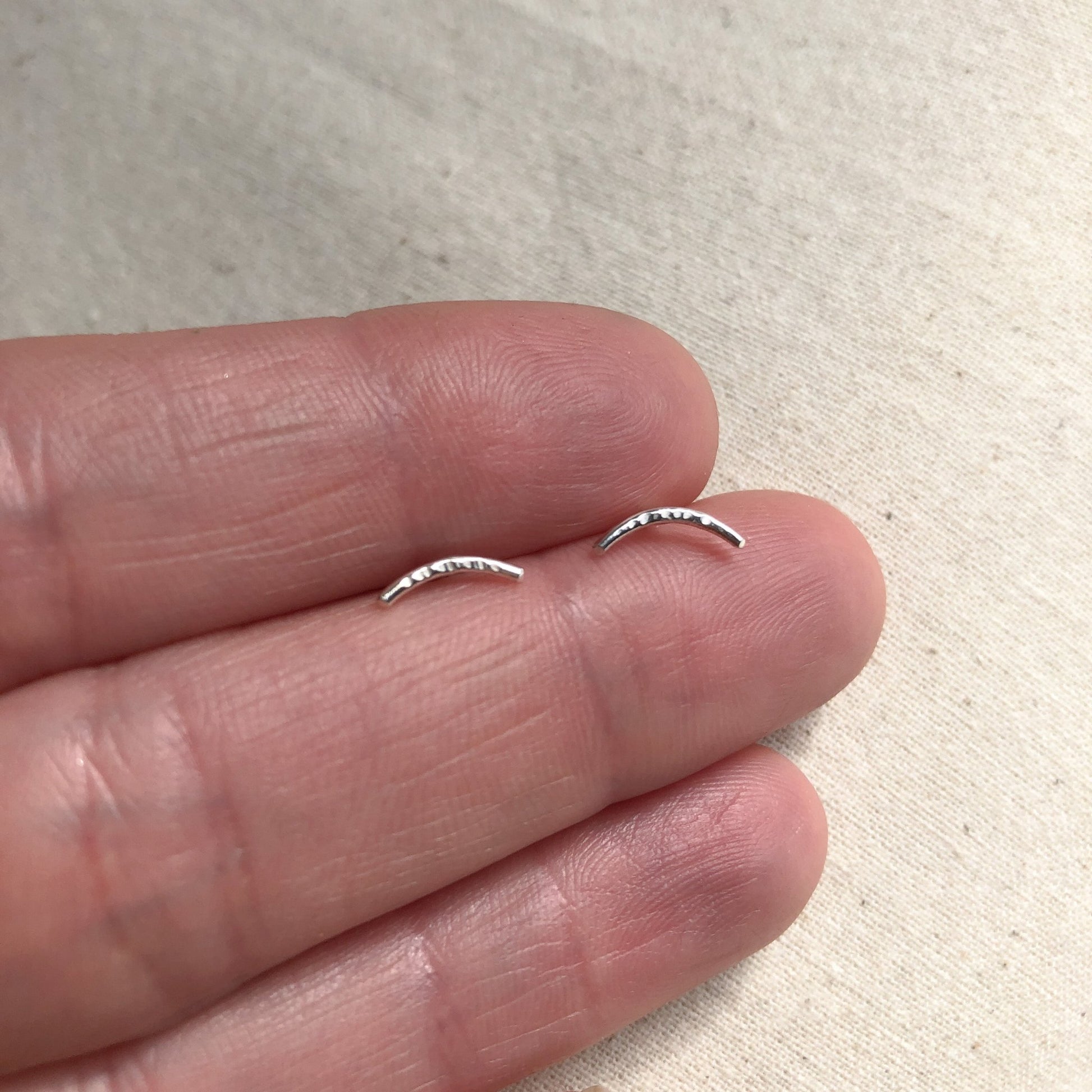 Curved sterling silver bar stud earrings in model's hand.