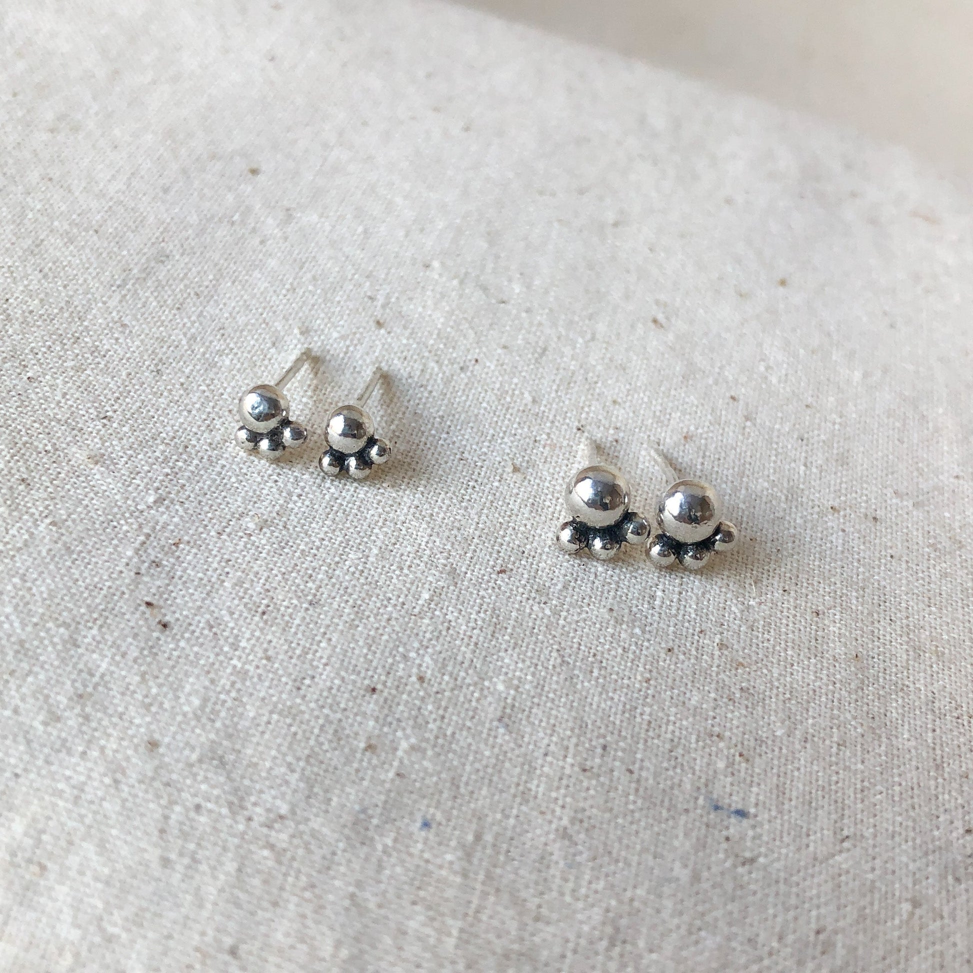 Two pair of silver ball stud earrings on grey background.