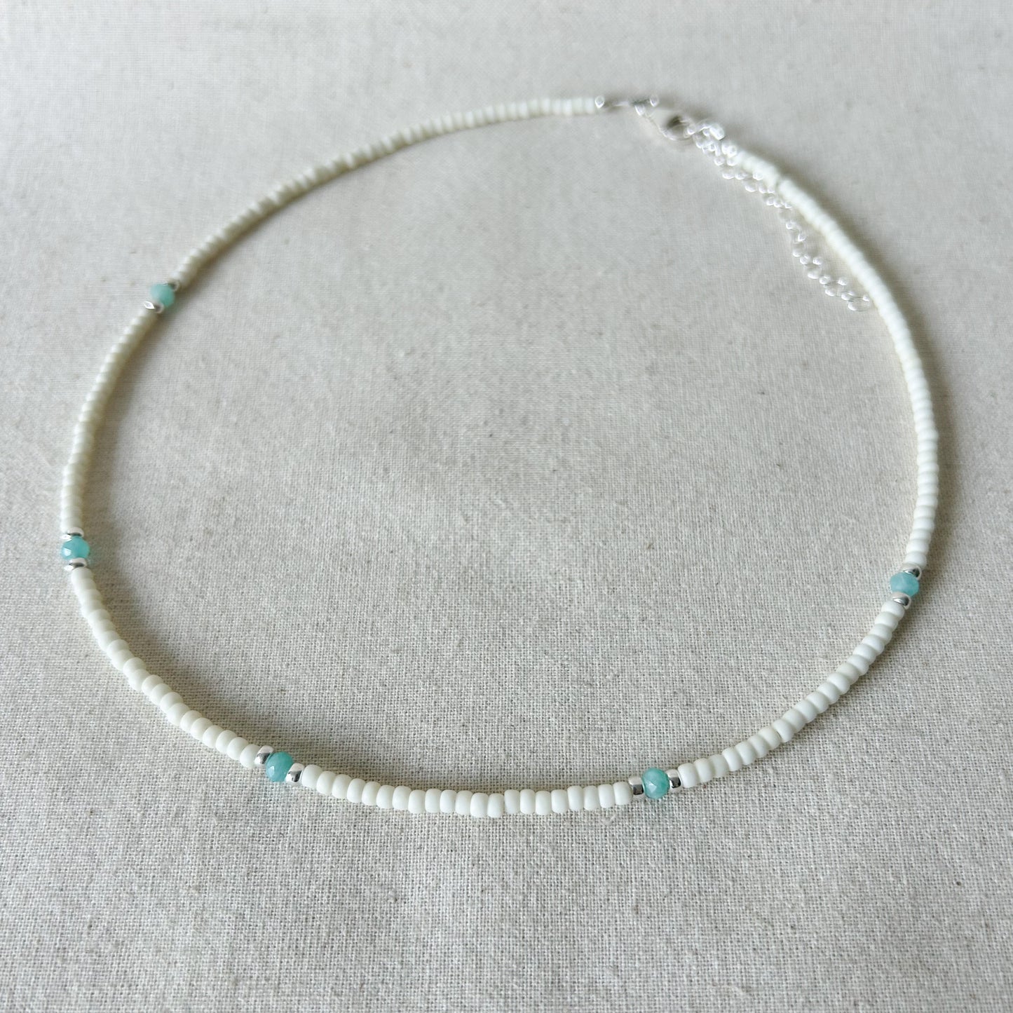 Necklace with white beads and turquoise accents on a light gray background