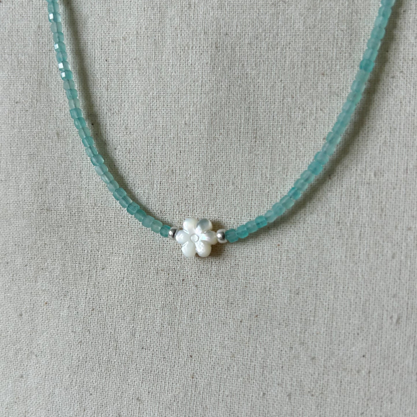 Necklace with turquoise beads and a white flower-shaped clasp on a gray fabric background
