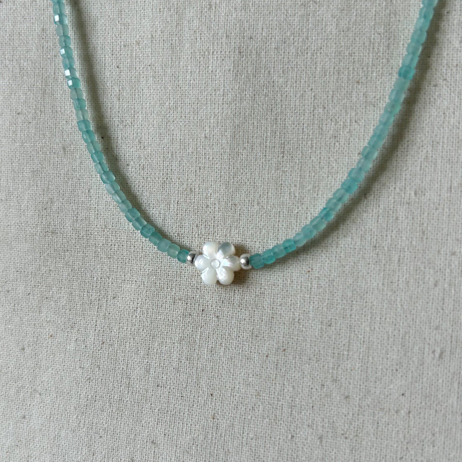 Necklace with turquoise beads and a white flower-shaped clasp on a gray fabric background