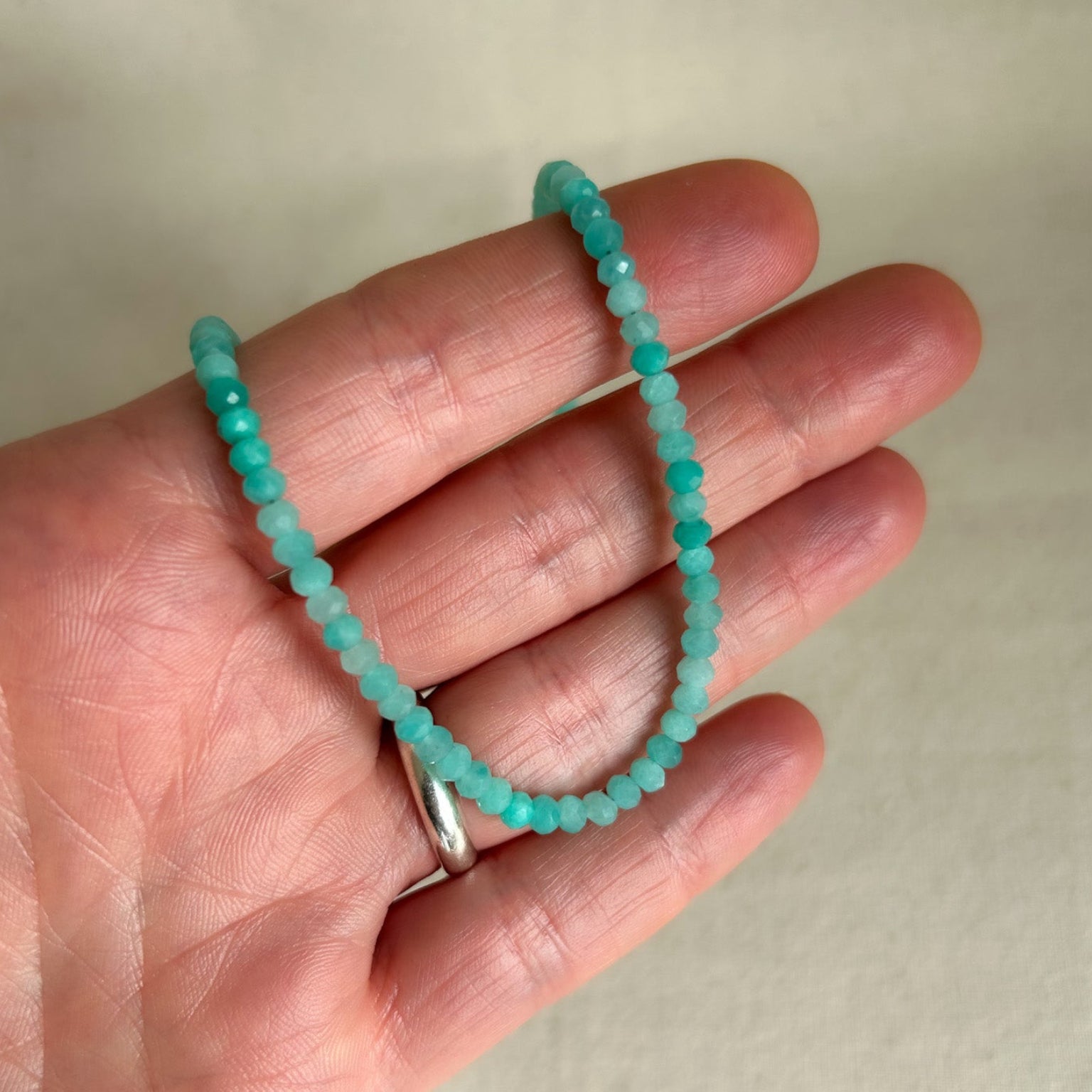 Turquoise colored gemstone necklace held on hand