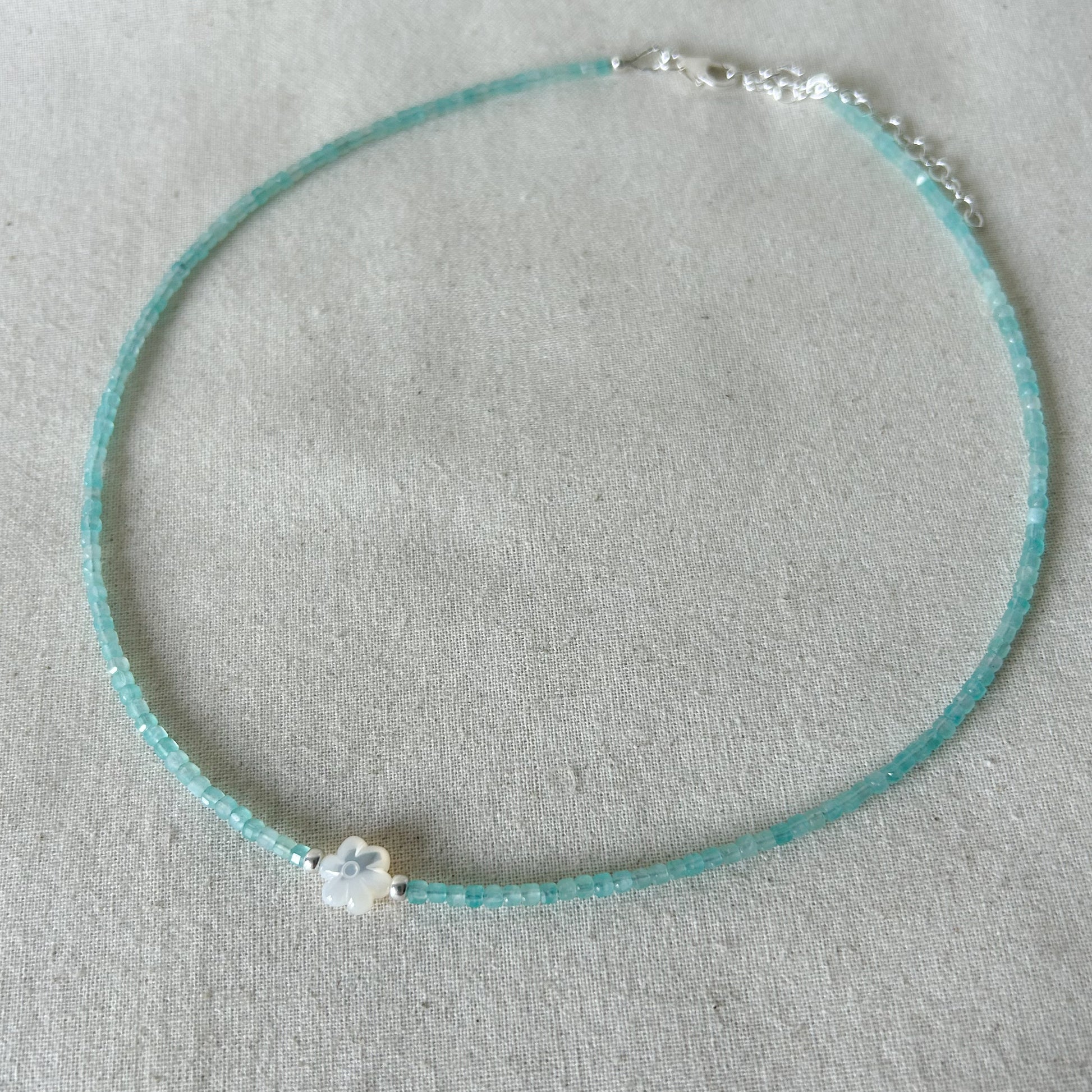 Turquoise beaded necklace with a small white flower pendant on a gray background