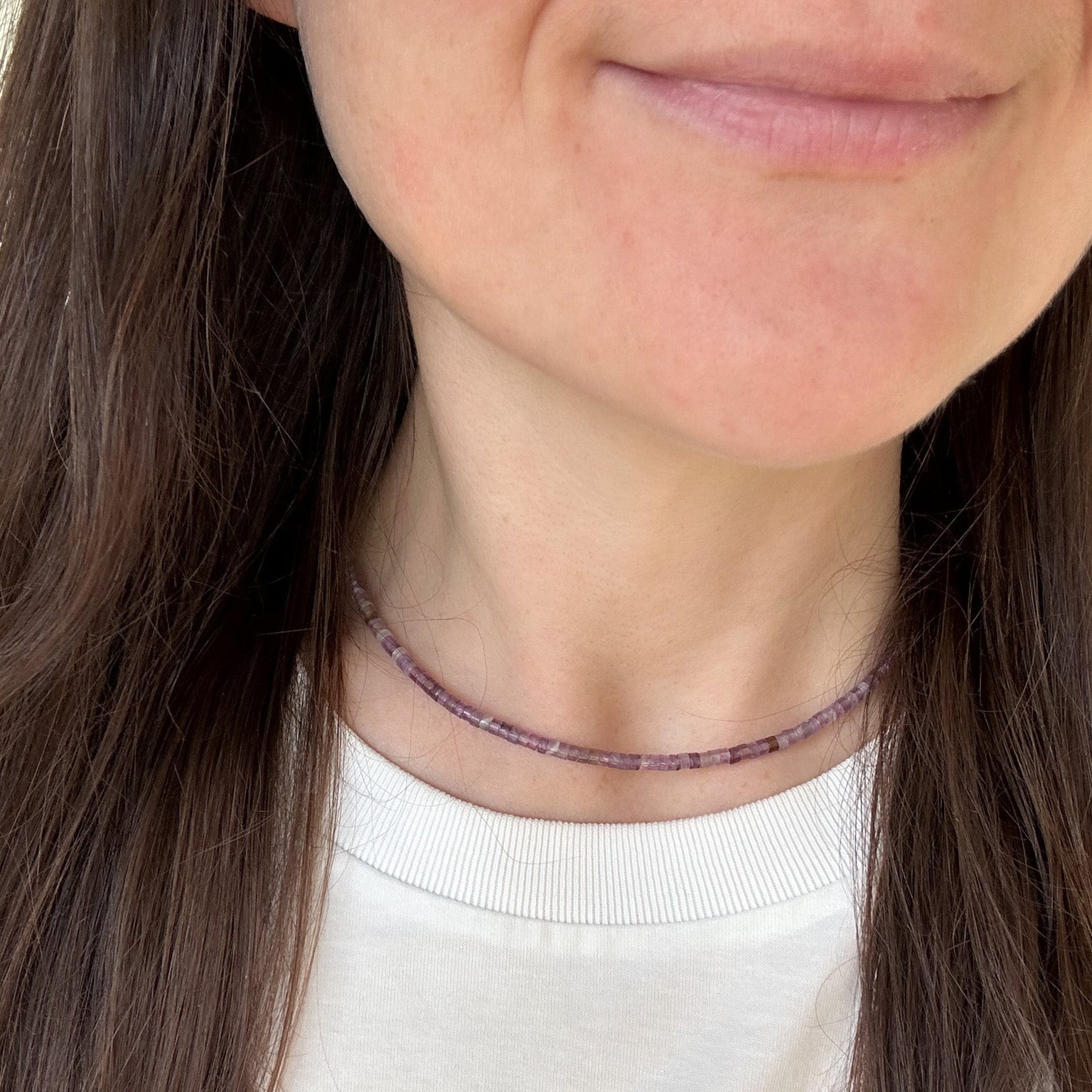 Close-up of a person wearing a delicate necklace with small beads.