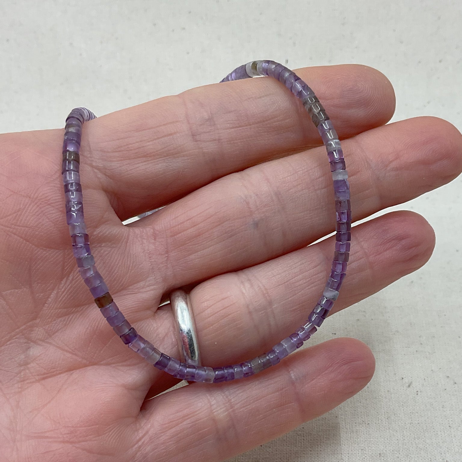 Purple beaded bracelet on a hand against a light background