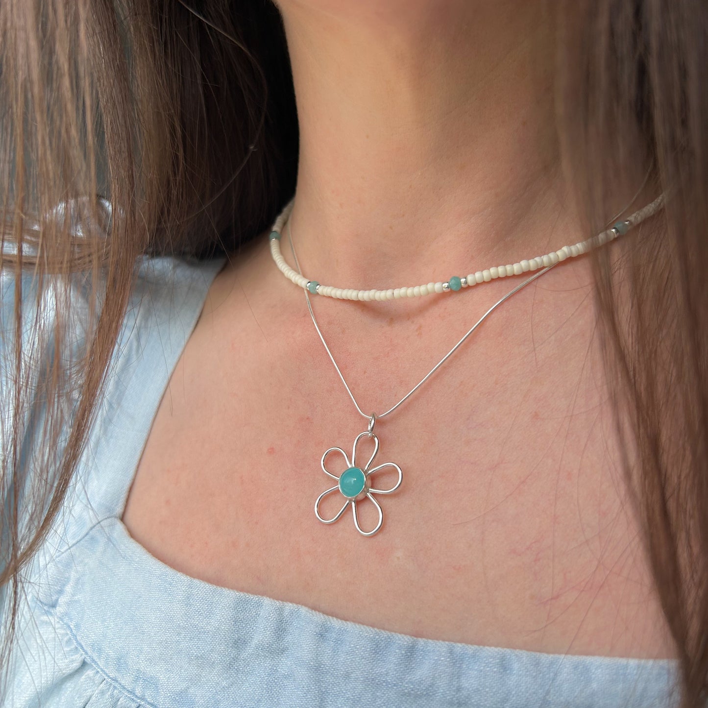 Flower necklace layered with beaded necklace being worn by model in blue shirt. 