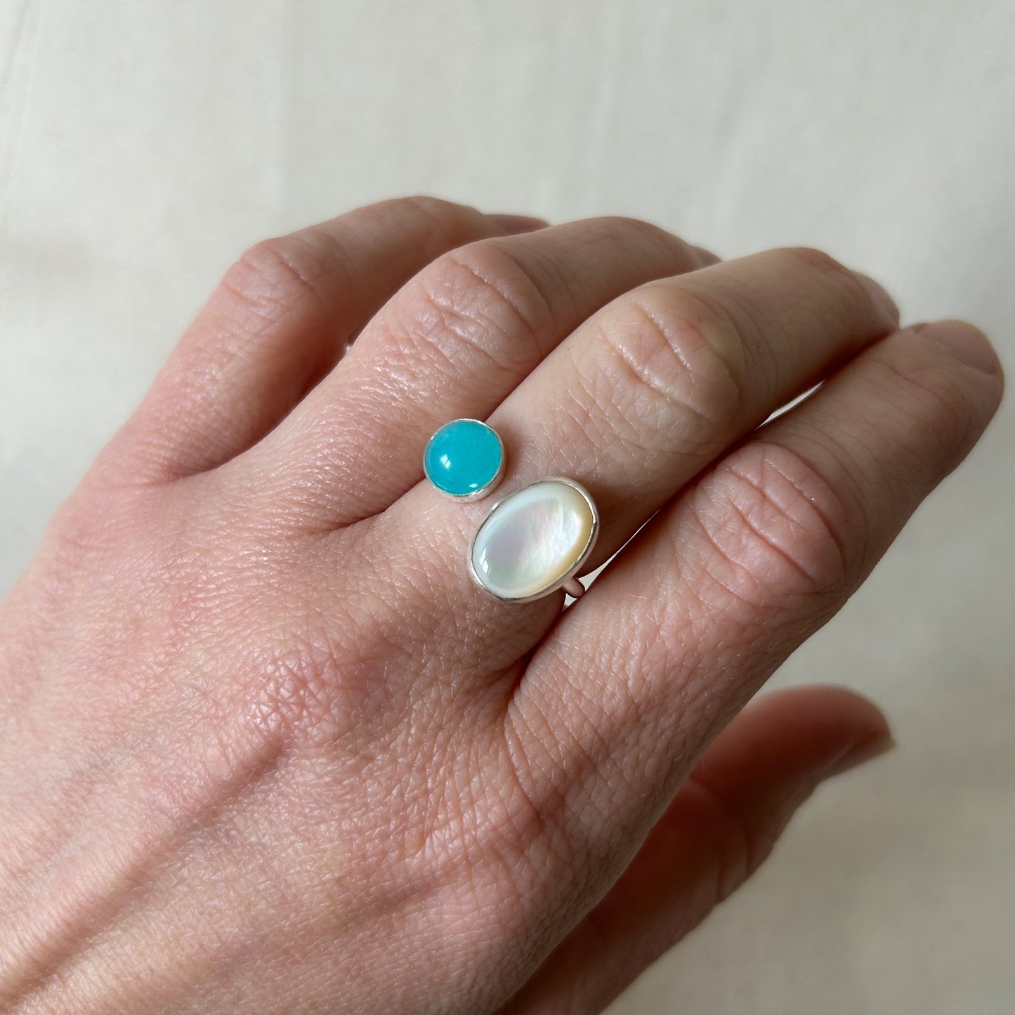 White oval stone ring with smaller blue stone on a gray background 