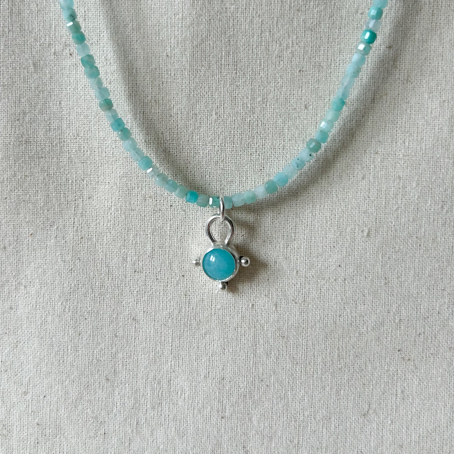 Turquoise beaded necklace with a silver pendant on a gray fabric background