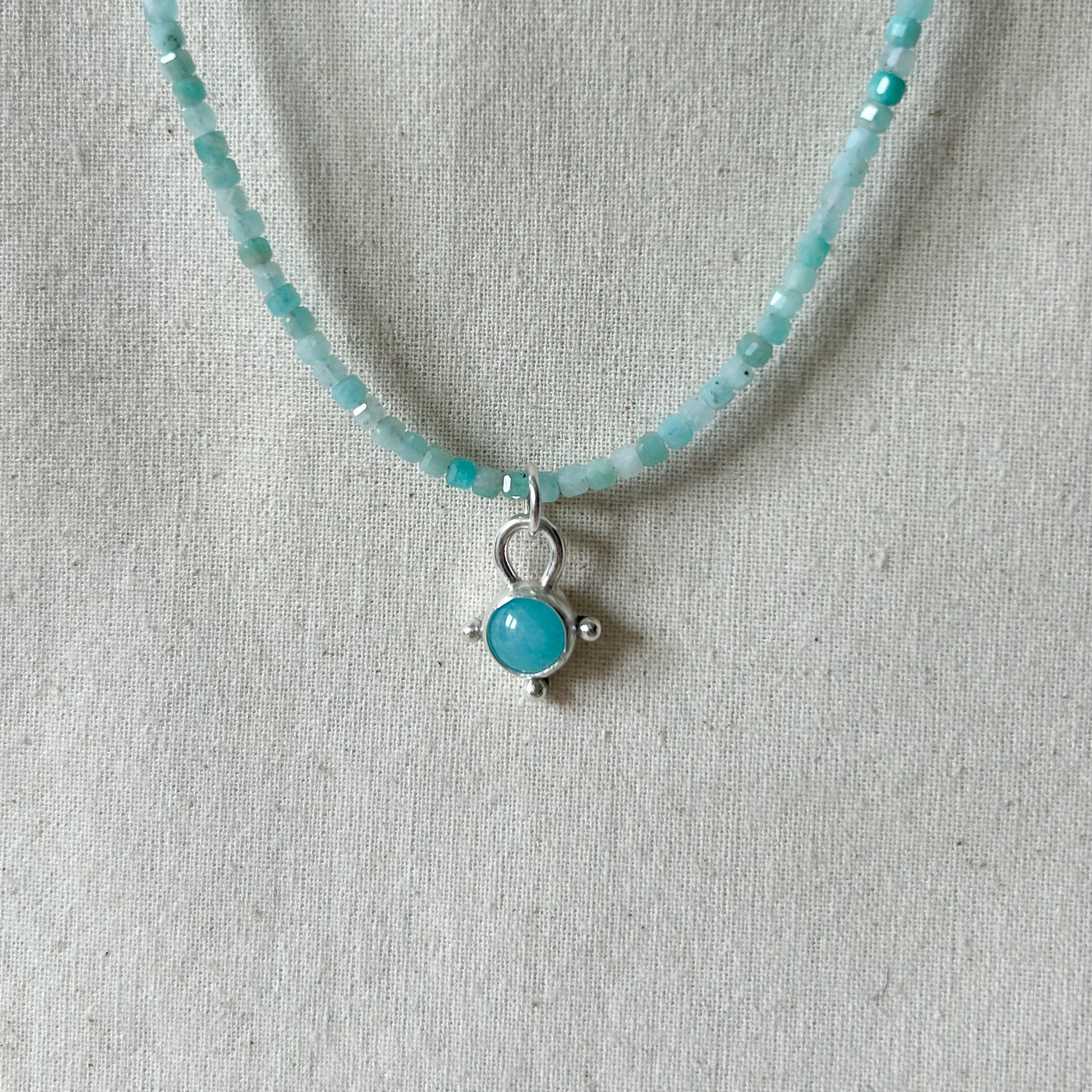 Turquoise beaded necklace with a silver pendant on a gray fabric background