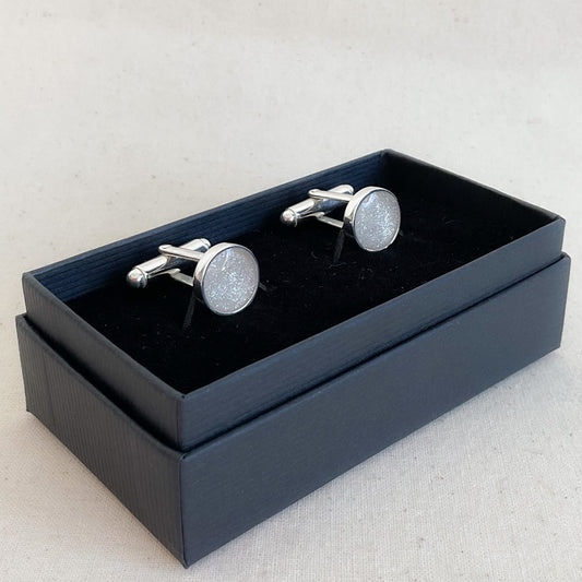 Round silver glittery cufflinks in a black box on a light gray background