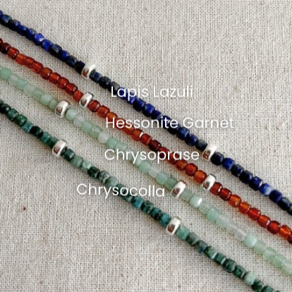 Four beaded bracelets labeled 'Lapis Lazuli', 'Hessonite Garnet', ‘Chrysoprase’ and 'Chrysocolla' on a textured fabric background.