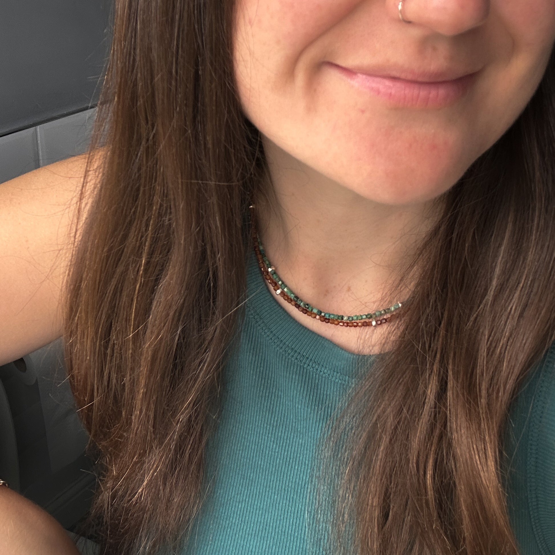 Close-up of a person with long brown hair wearing a green top and beaded necklaces