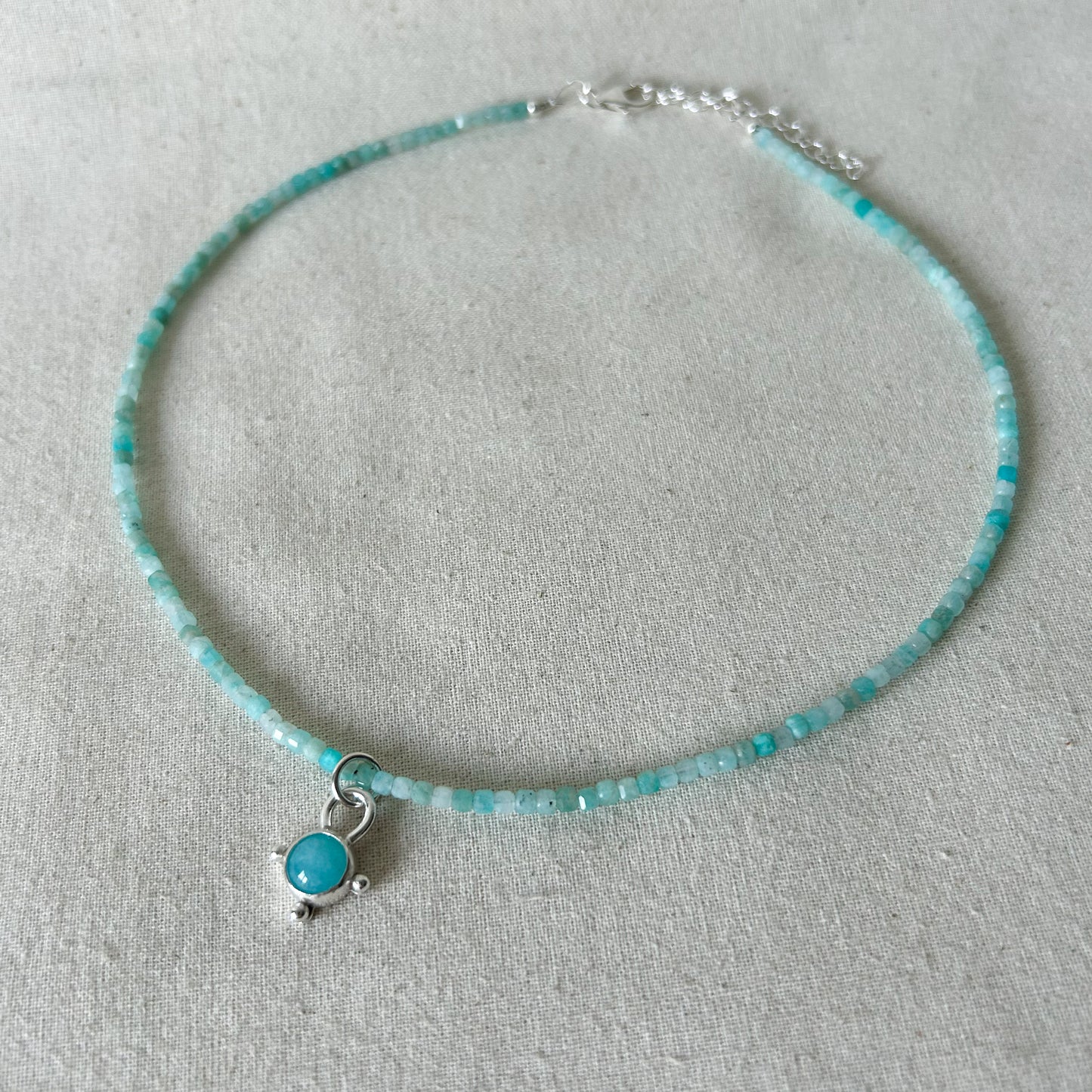 Turquoise beaded necklace with a silver charm on a light gray background