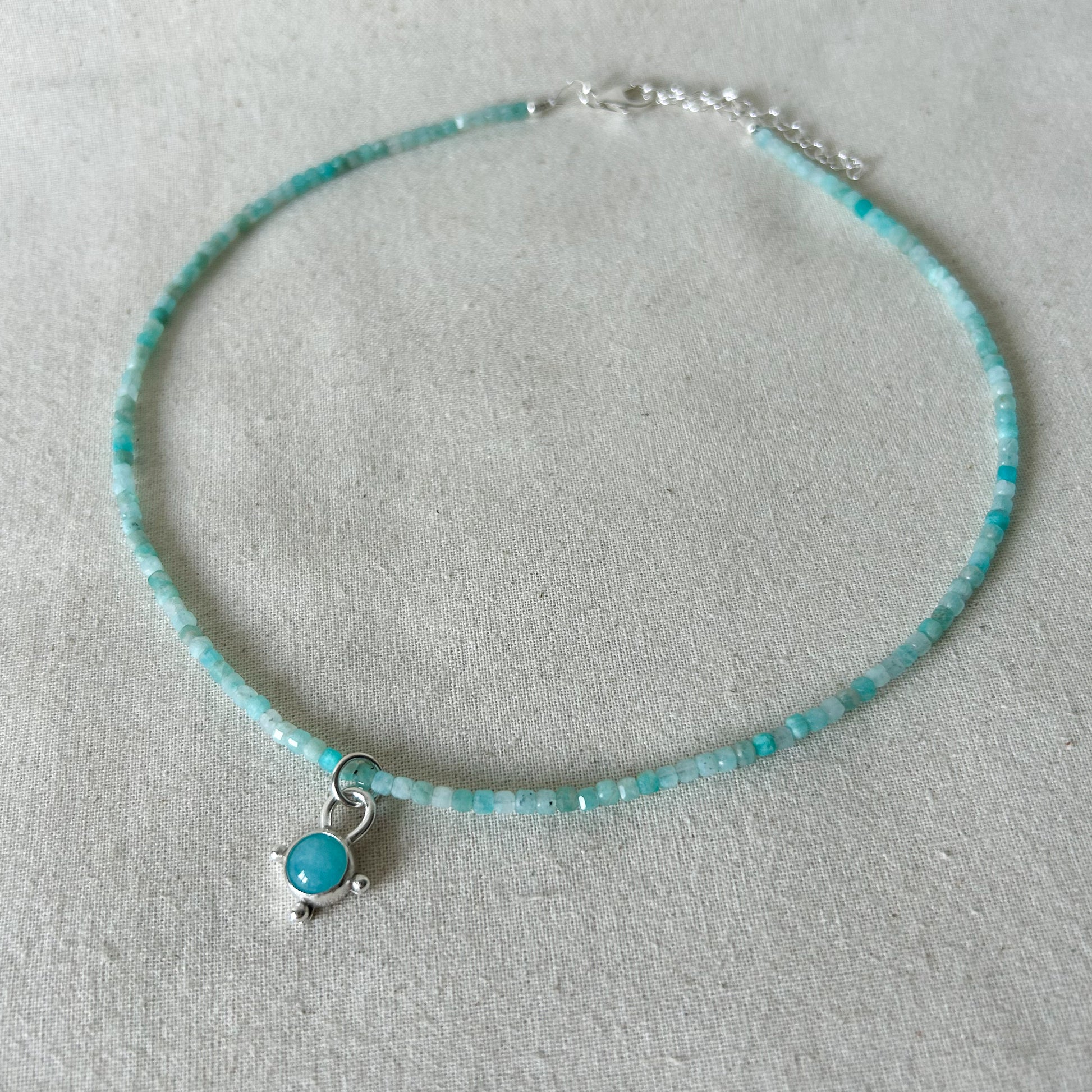 Turquoise beaded necklace with a silver charm on a light gray background