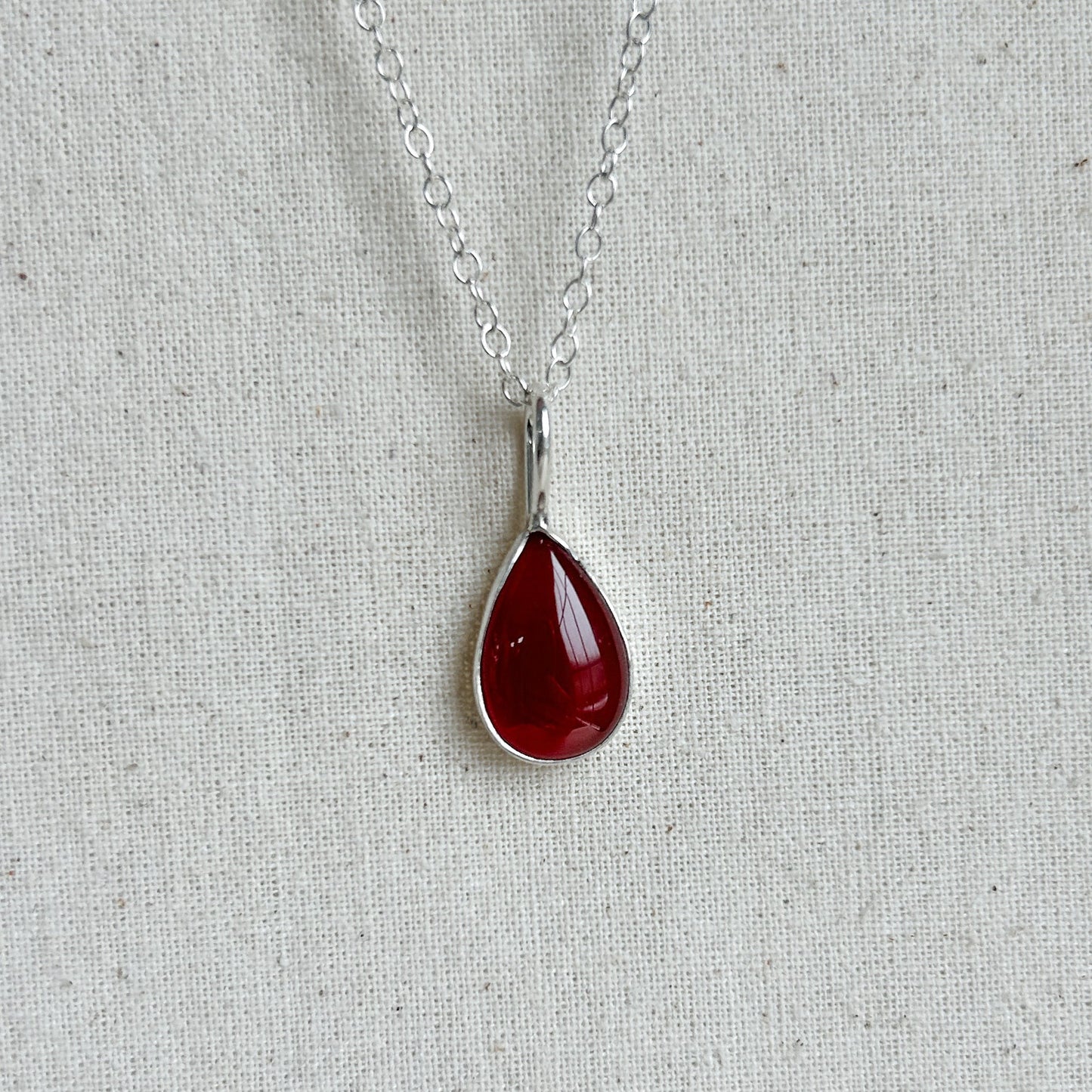 Teardrop-shaped red pendant on a silver chain against a light gray background