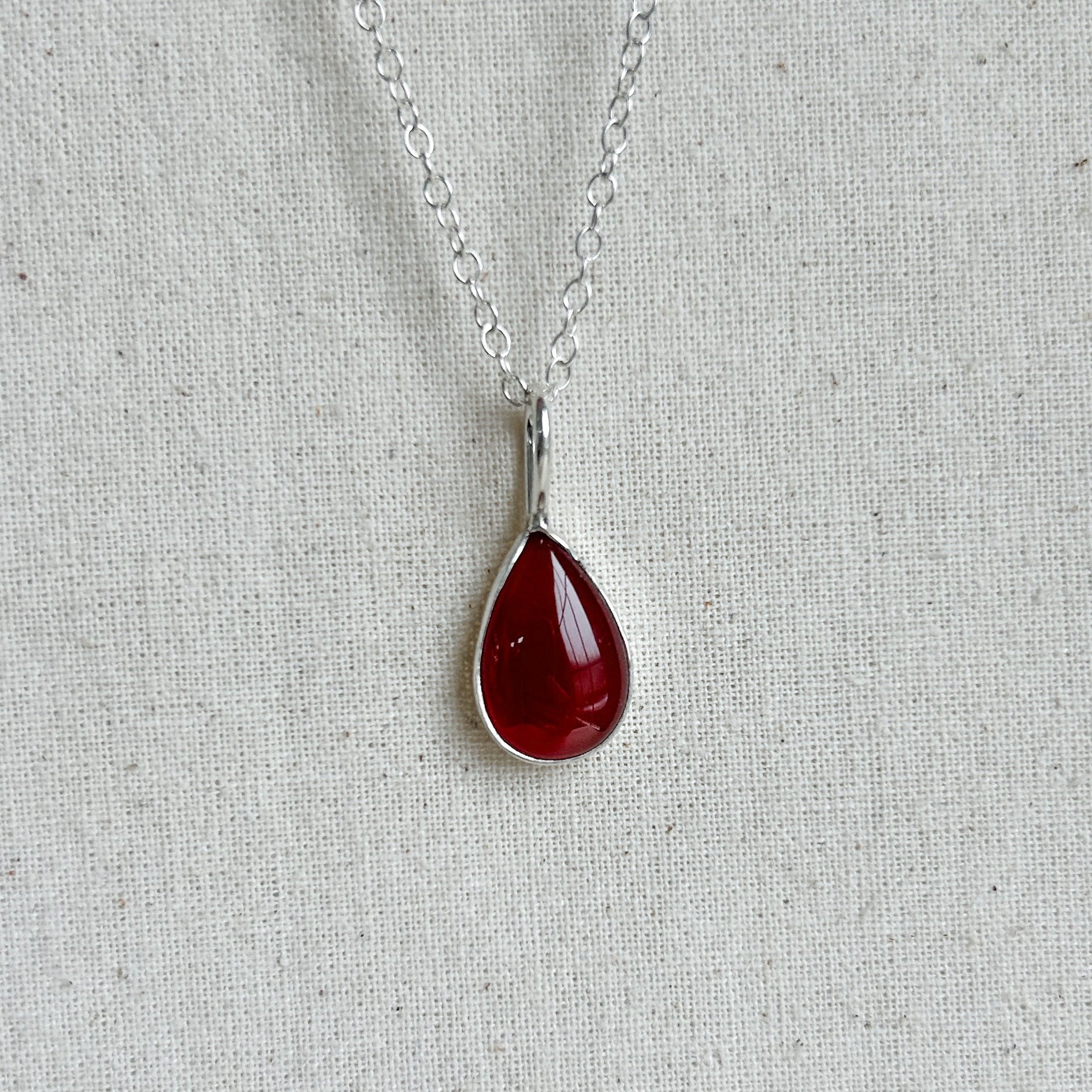 Teardrop-shaped red pendant on a silver chain against a light gray background