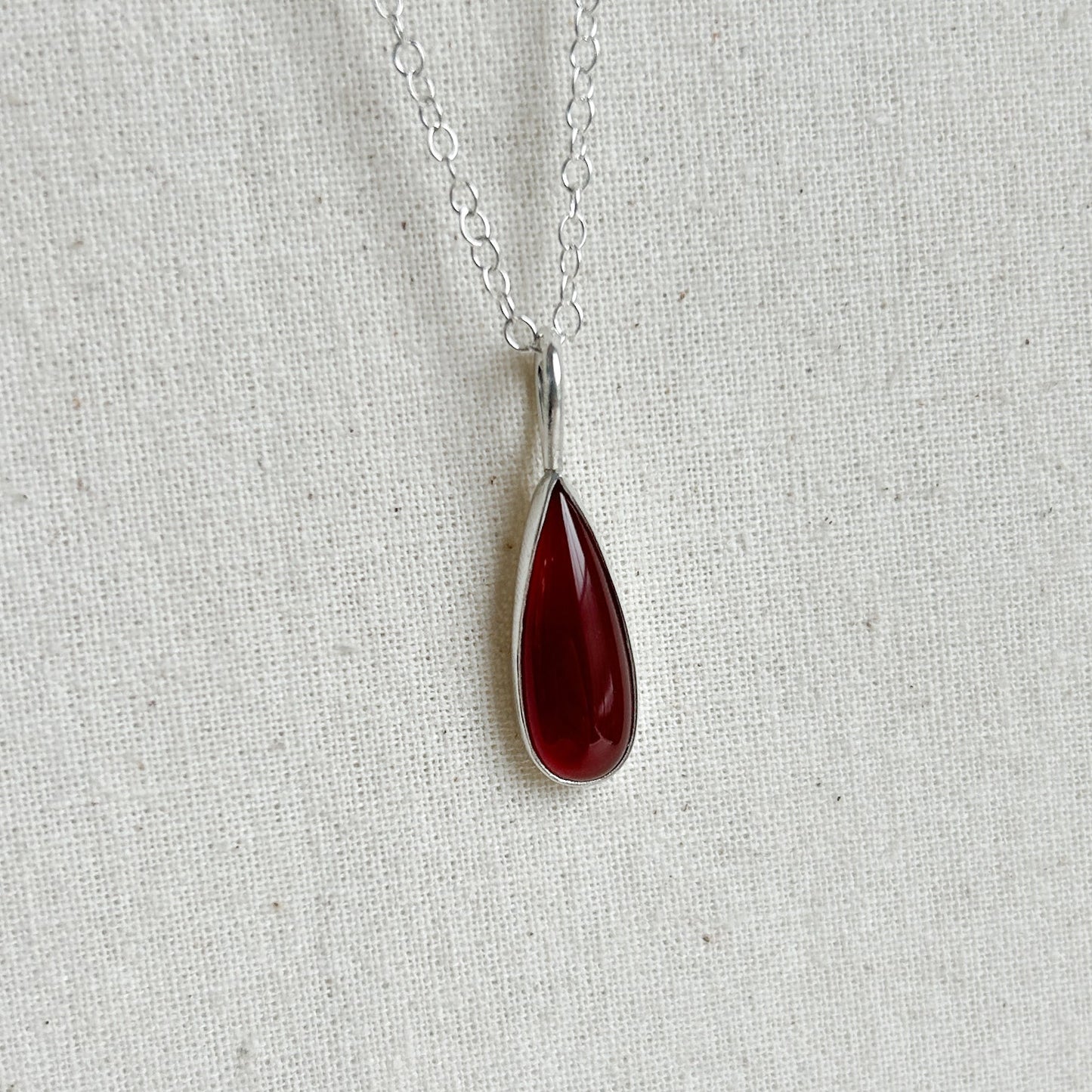 Teardrop-shaped red pendant on a silver chain against a light gray background