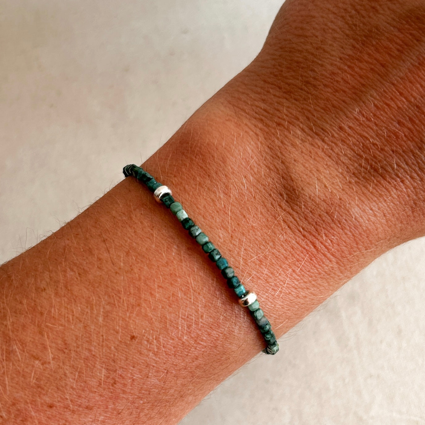 Green beaded bracelet on a wrist against a neutral background