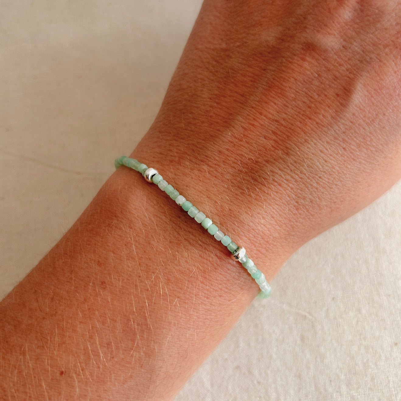 Close-up of a wrist wearing a green beaded bracelet on a neutral background