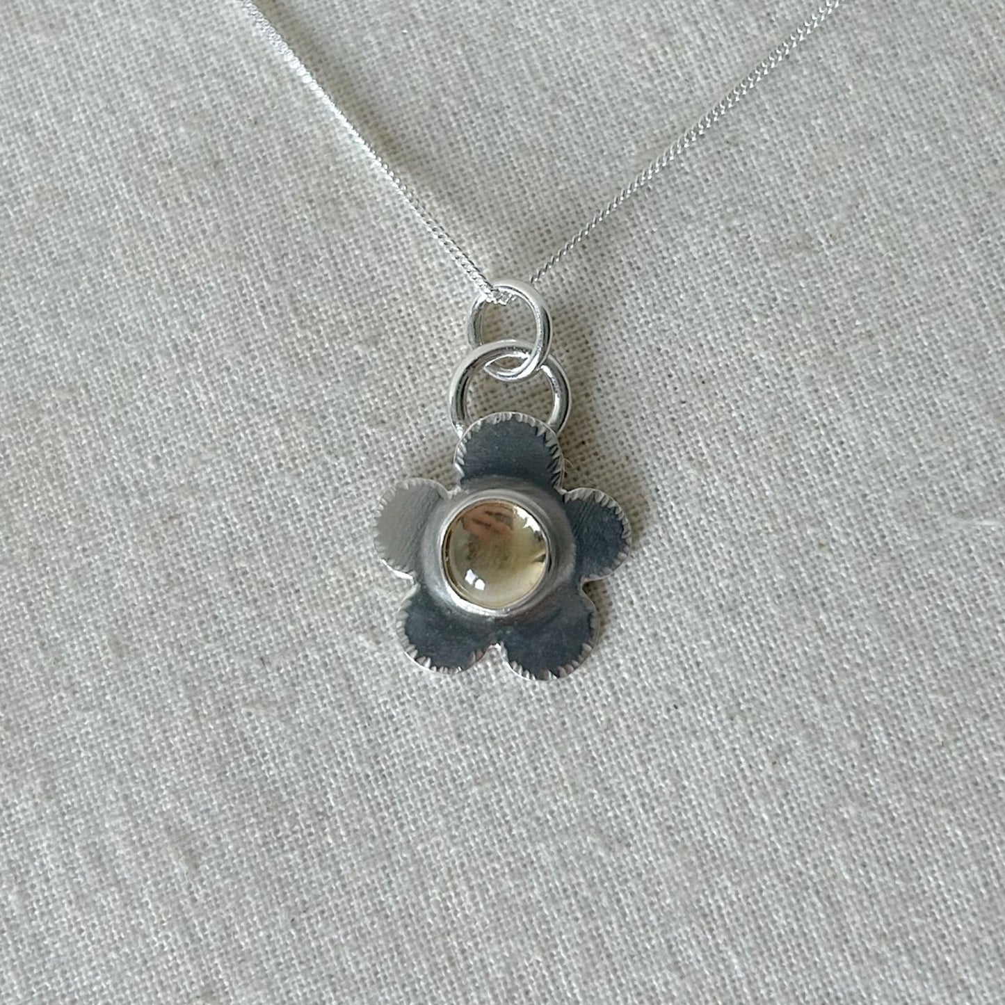 Silver pendant with a central gemstone on a light gray fabric background