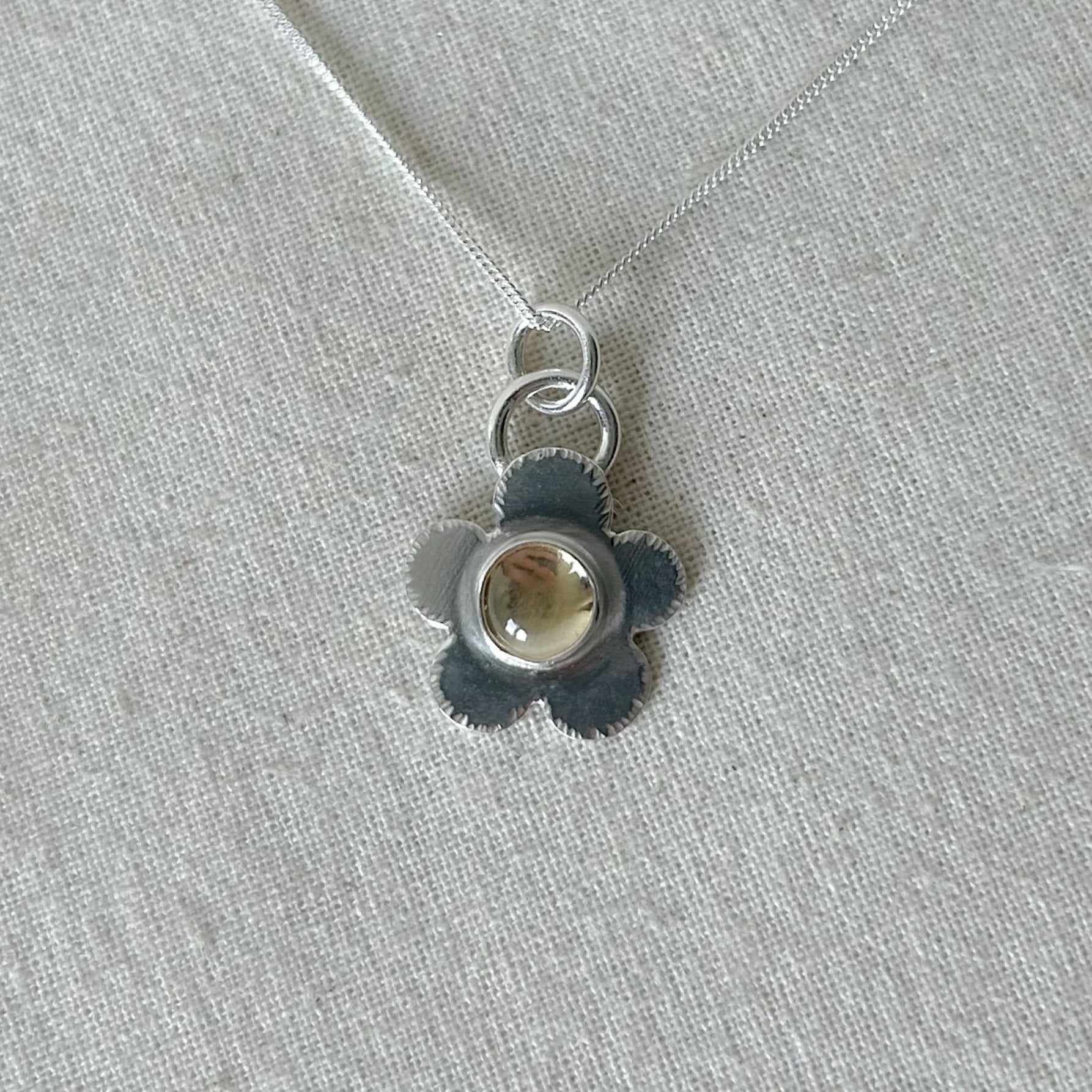 Silver pendant with a central gemstone on a light gray fabric background