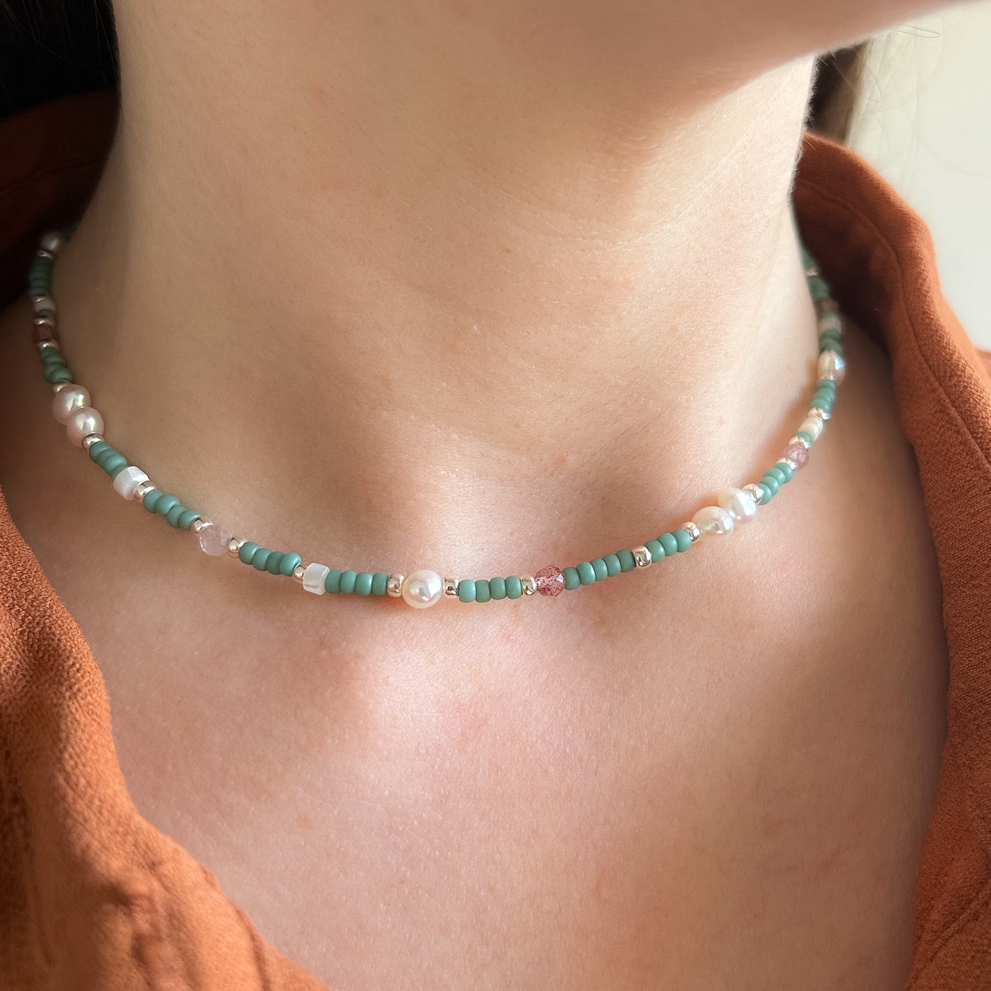 Necklace with green beads and pearls on a person wearing an orange top.