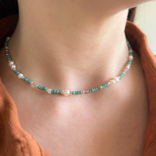 Necklace with green beads and pearls on a person wearing an orange top.