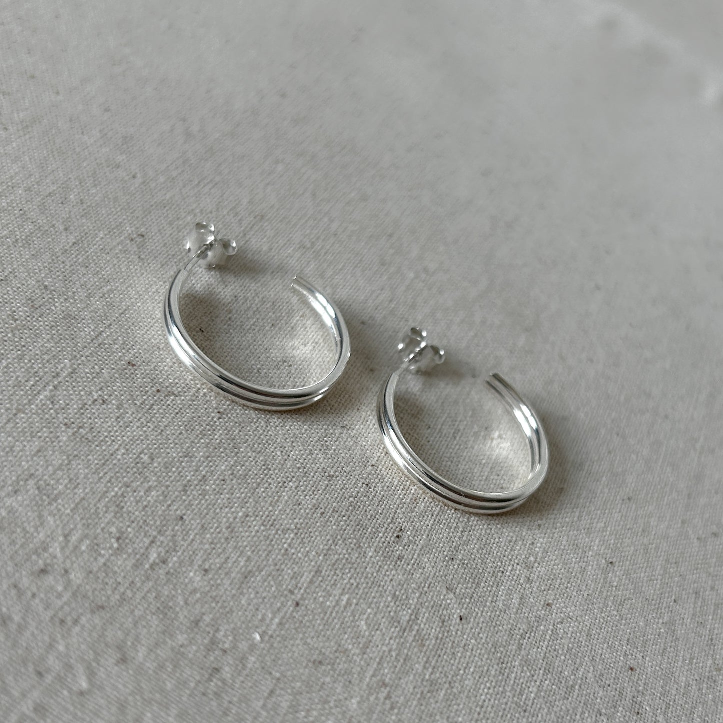Two small silver ear huggies on a grey background