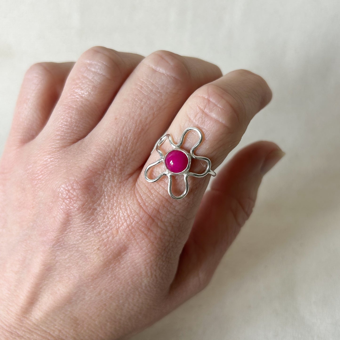 Silver flower shaped ring with pink stone with a grey background 