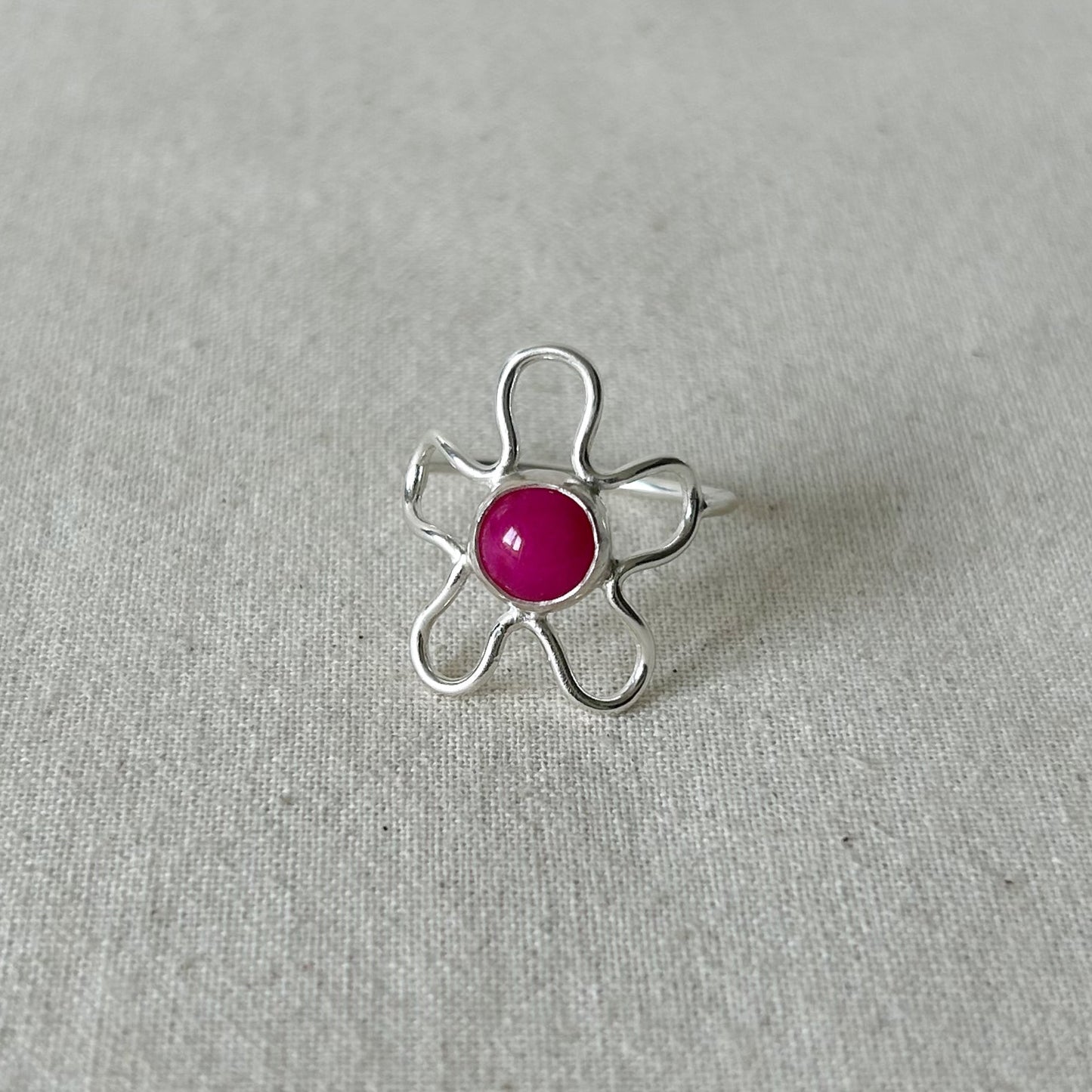 Silver flower shaped ring with pink stone on a grey background 