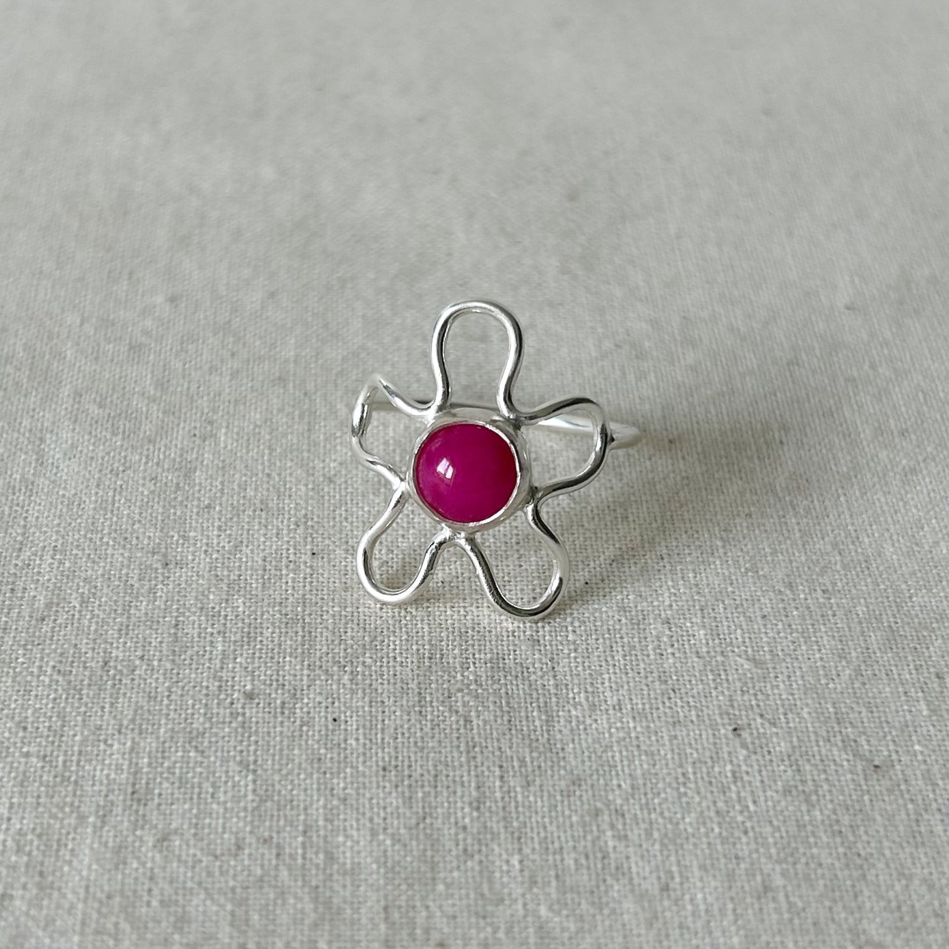 Silver flower shaped ring with pink stone on a grey background 