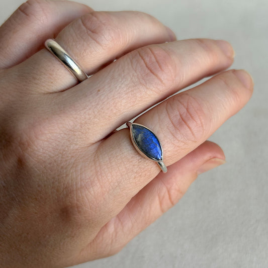 A close-up of a hand wearing a silver ring with a marquise-cut blue stone, alongside another simple silver band ring.