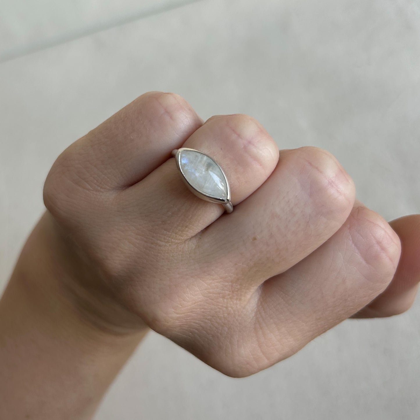 A close-up of a hand wearing a silver ring with a marquise-shaped iridescent white gemstone.