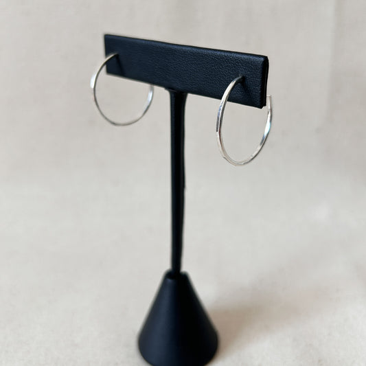 A pair of medium silver hoop earrings displayed on a black stand with a black background.