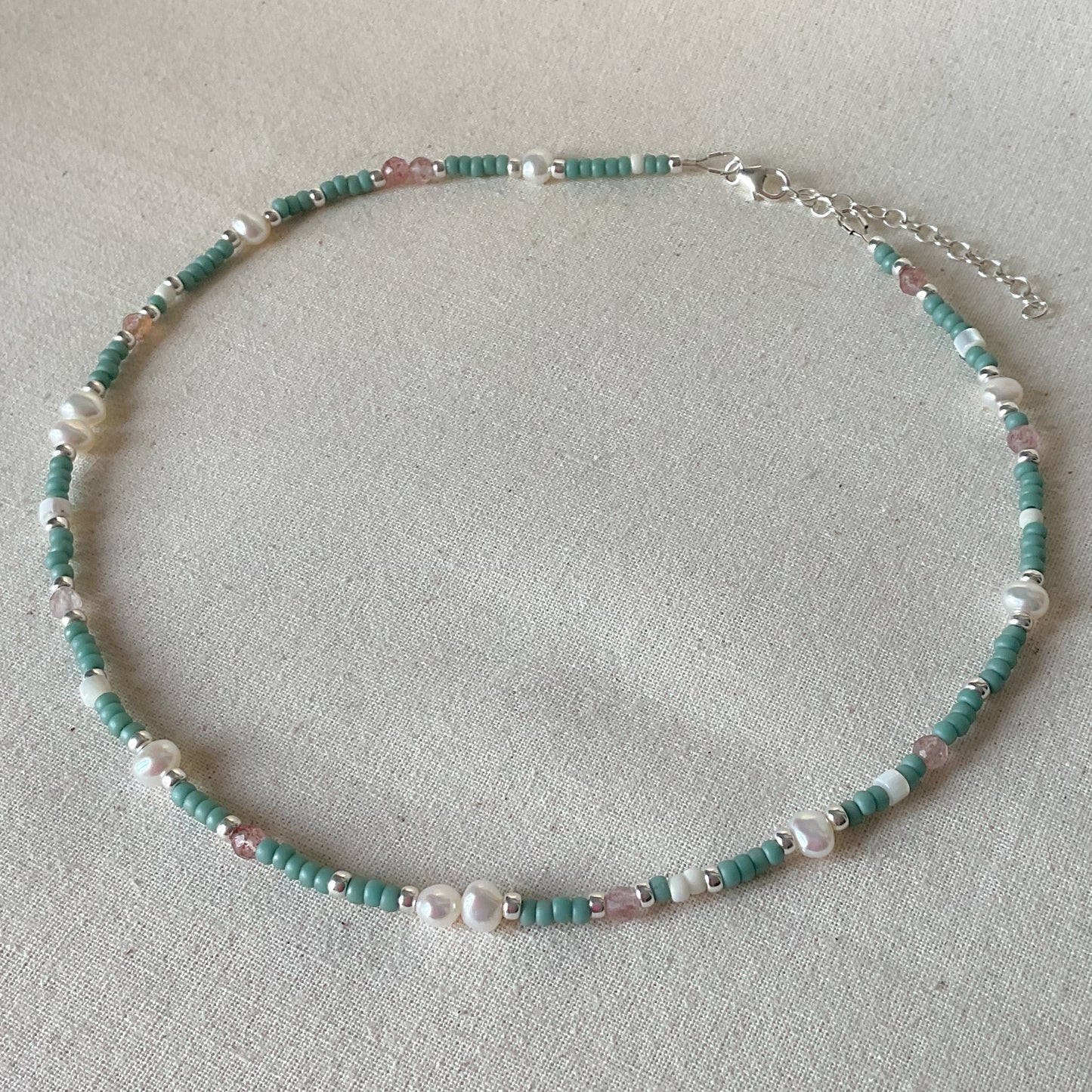 Beaded necklace with turquoise and white beads on a light gray background