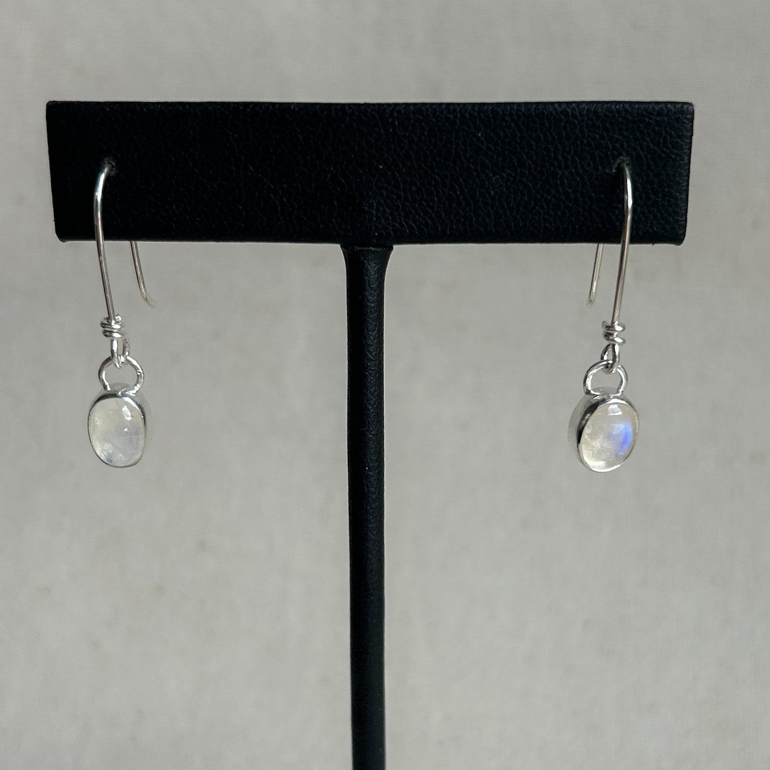 Pair of silver earrings with moonstone drops on a black earring stand against a gray background