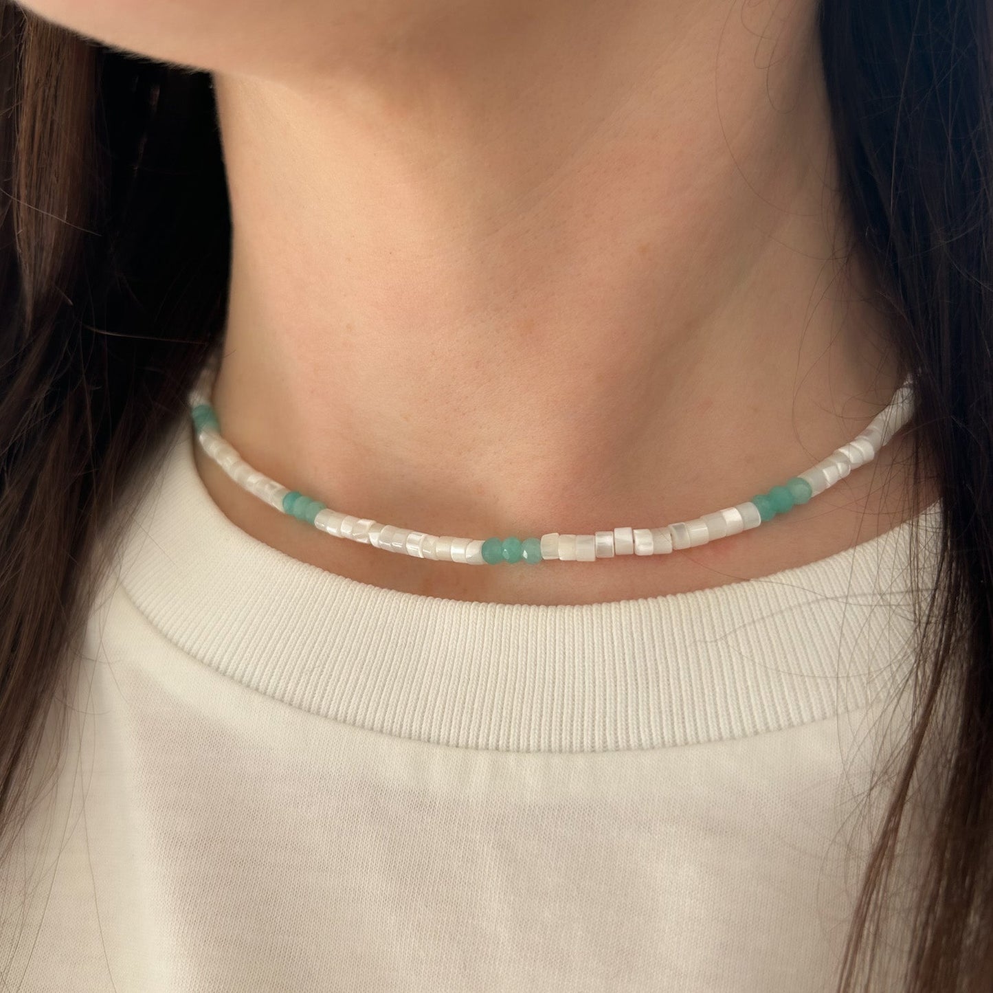 Necklace with turquoise and white beads worn by a person in a beige sweater.
