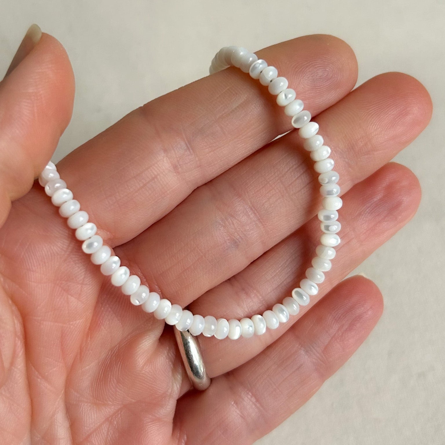 White beaded bracelet with a silver clasp on a hand against a beige background