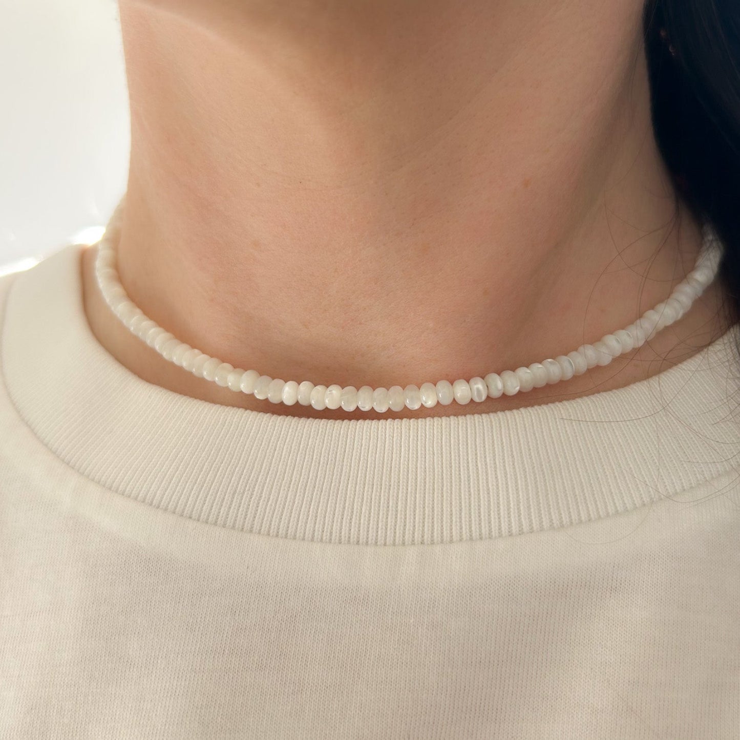 Close-up of a person wearing a delicate beaded necklace against a neutral background
